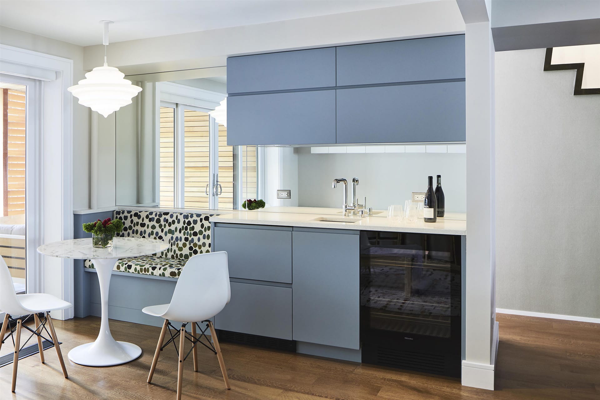 Wet bar with blue millwork and banquette, white table and chairs and modern pendant light.