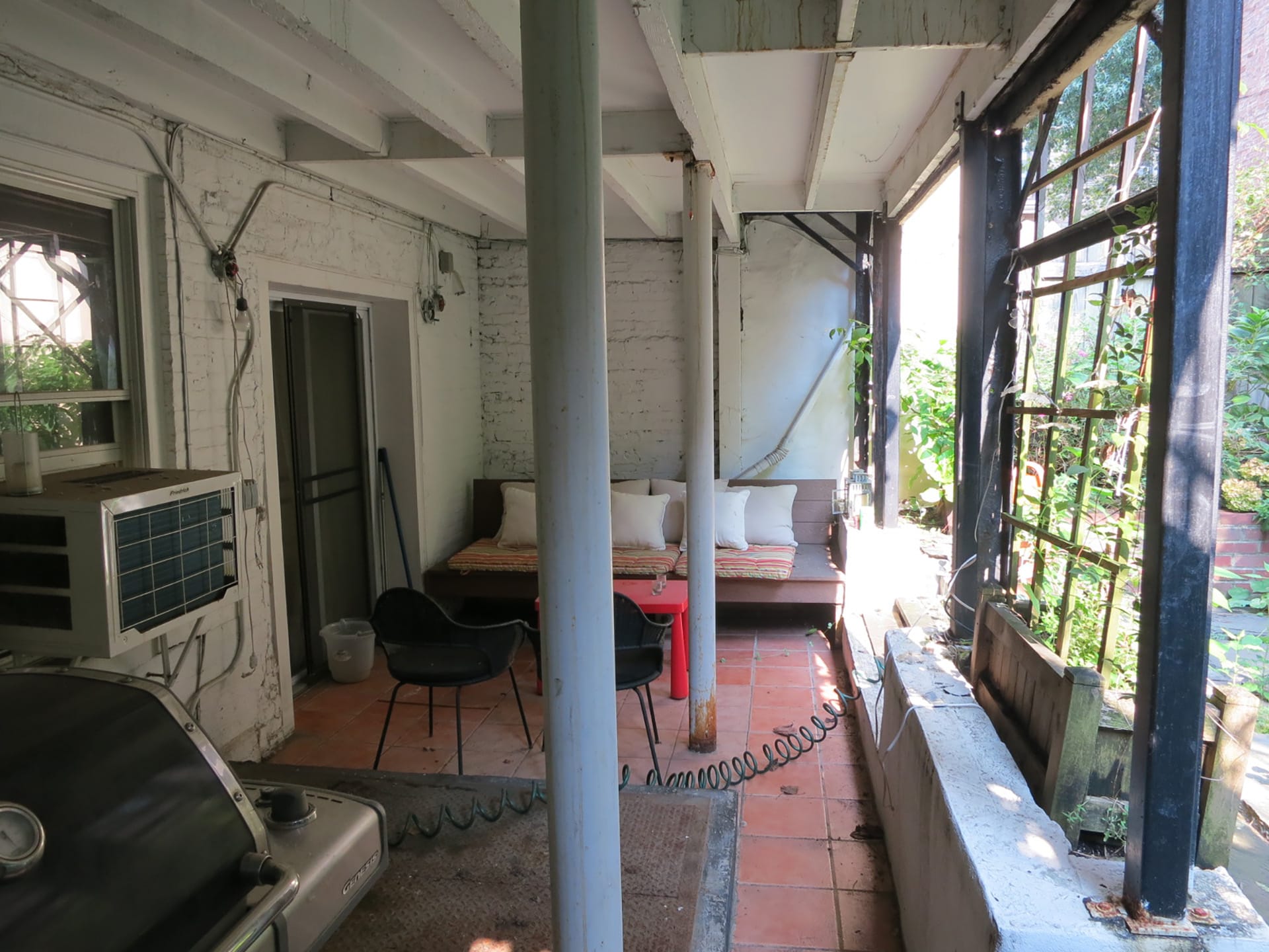 Areaway before our renovation with faded white-painted brick and wood, two support columns, and a trellis