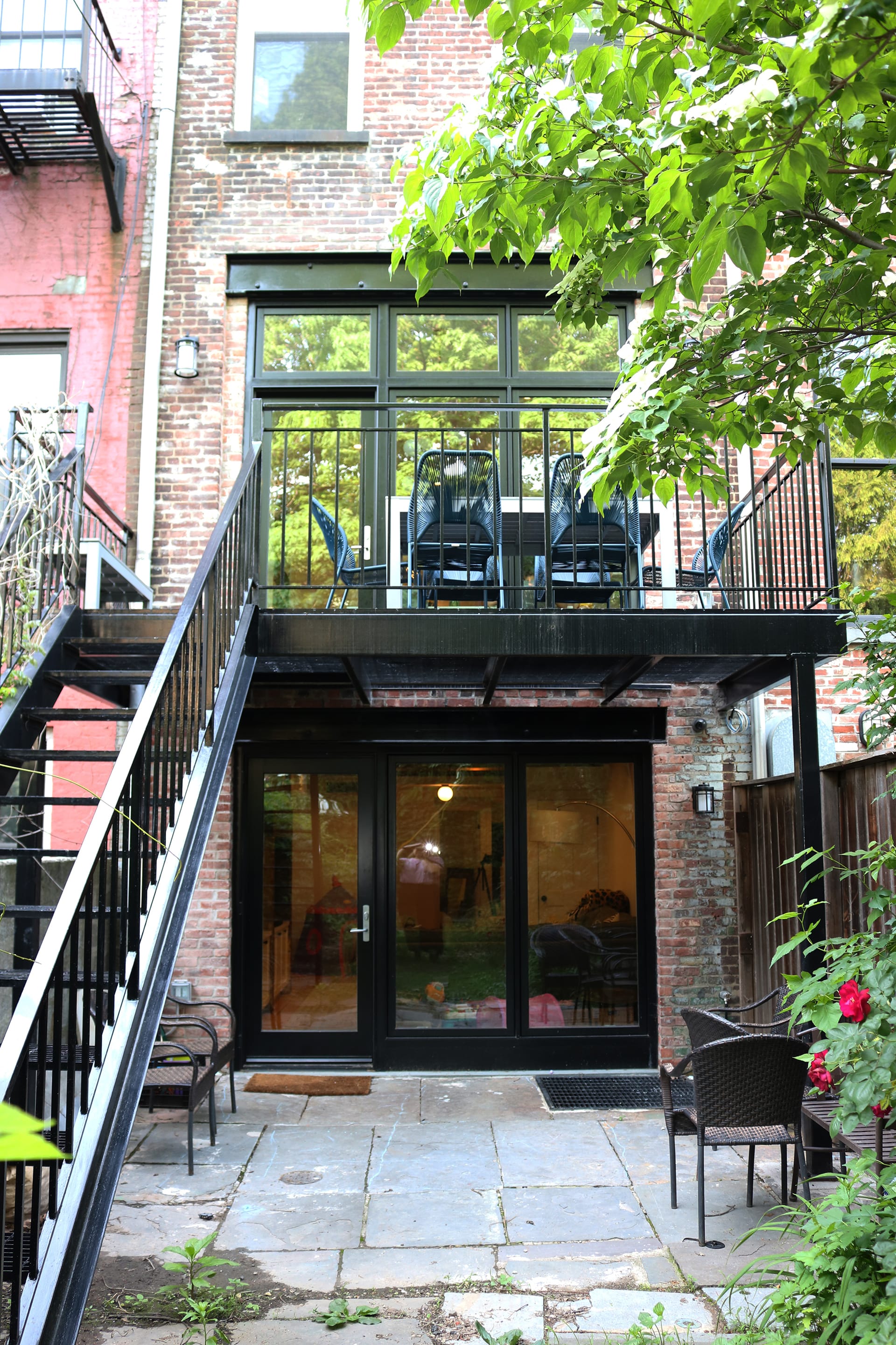 Rear facade of Cobble Hill townhouse after renovation with two sets of large glass doors, one on the ground level and one leading to a second-story outdoor deck.