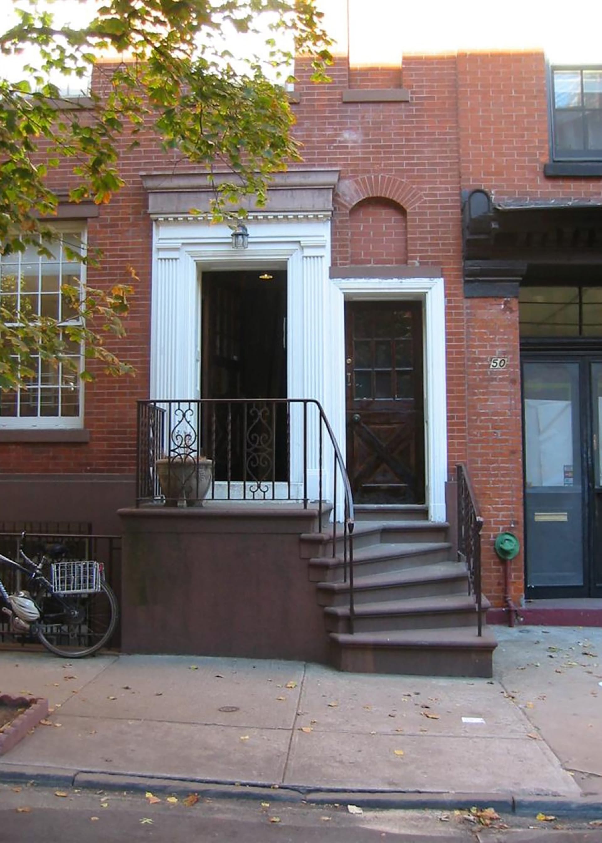 Stoop prior to renovation. Two dark brown front doors sit next to each other, with white framing. A stoop with staircase to the right sits in front of the doors.