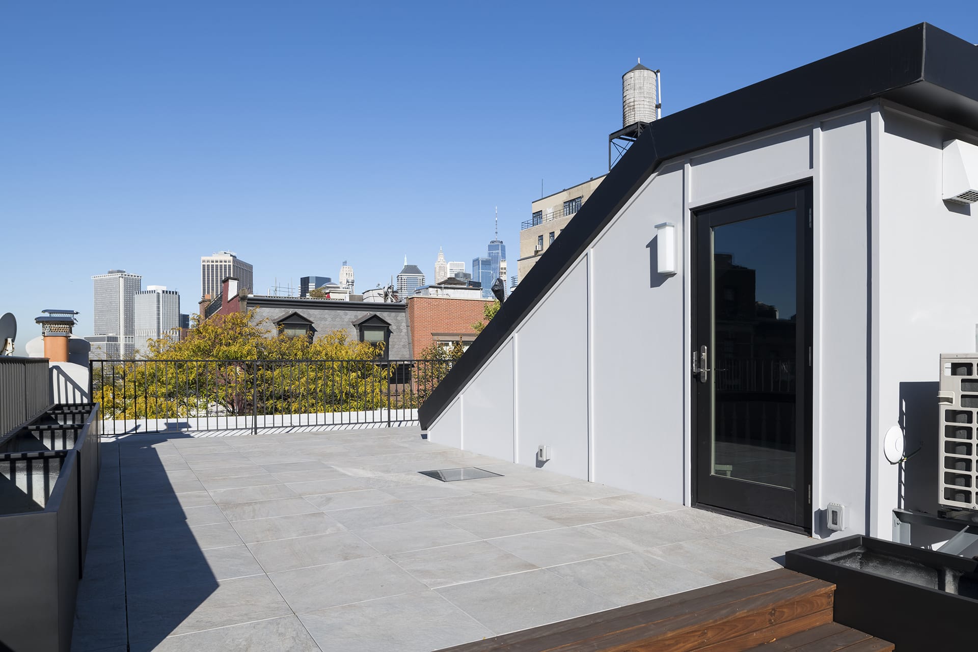 Rooftop after renovation, with new bulkhead, bluestone pavers, and wooden steps