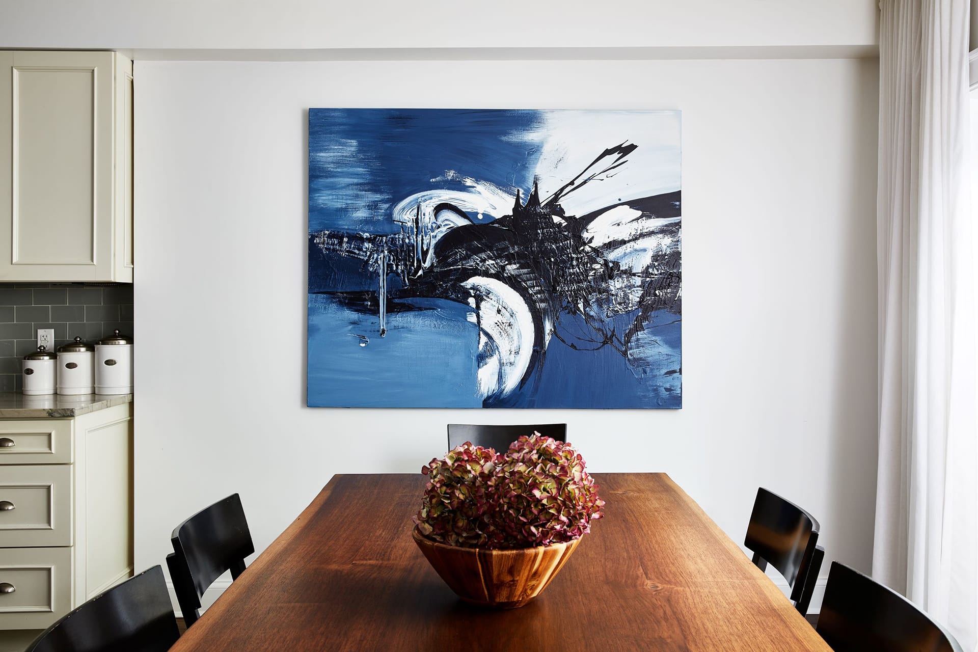 Dining area with a natural wood table and large blue painting on the wall.