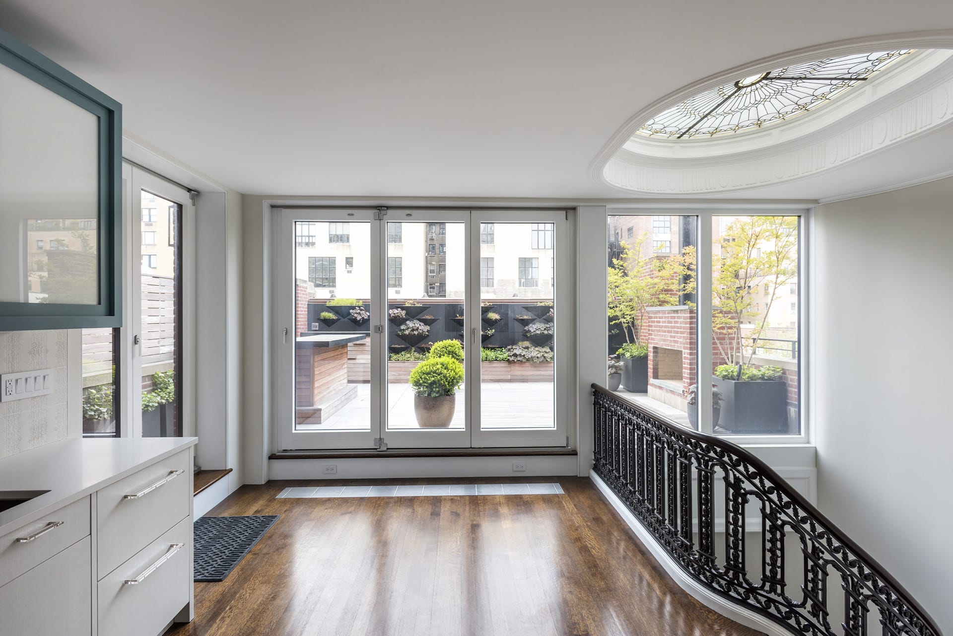 Interior of an Upper West Side penthouse with a view onto the roof deck through large folding glass doors. A large leaded glass skylight is located at the right of the frame.