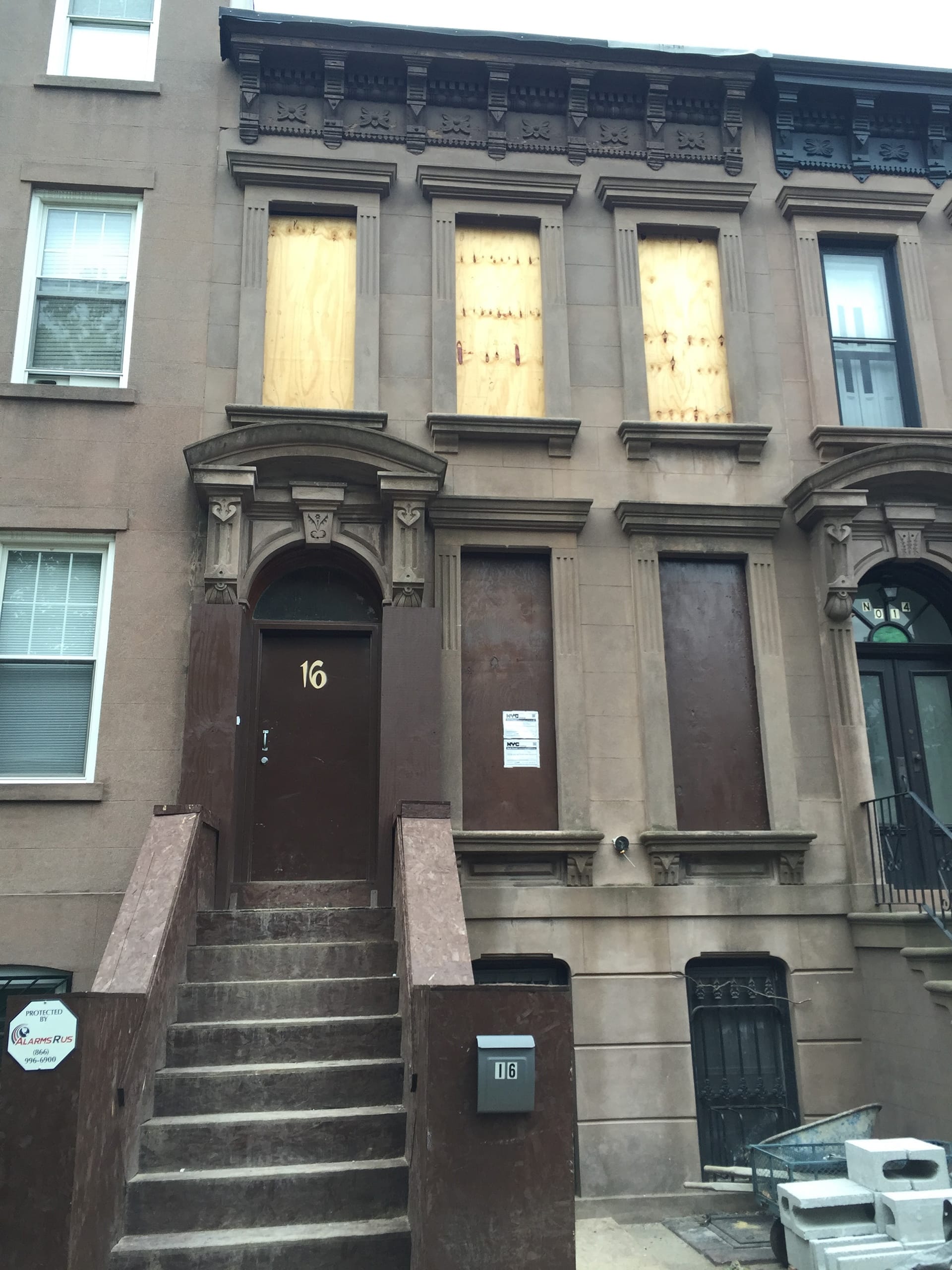 Front facade of a townhouse during construction with all windows boarded up with plywood