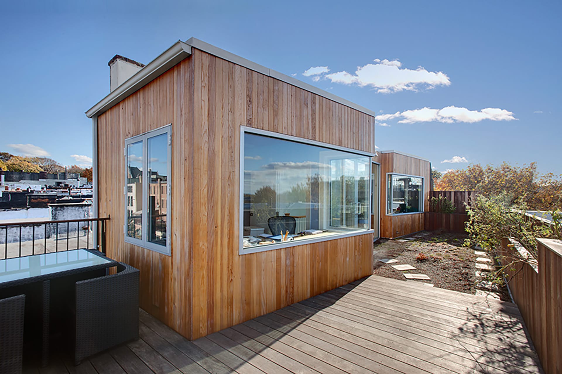 Exterior of a townhouse penthouse with wood siding and large glass windows and glass doors