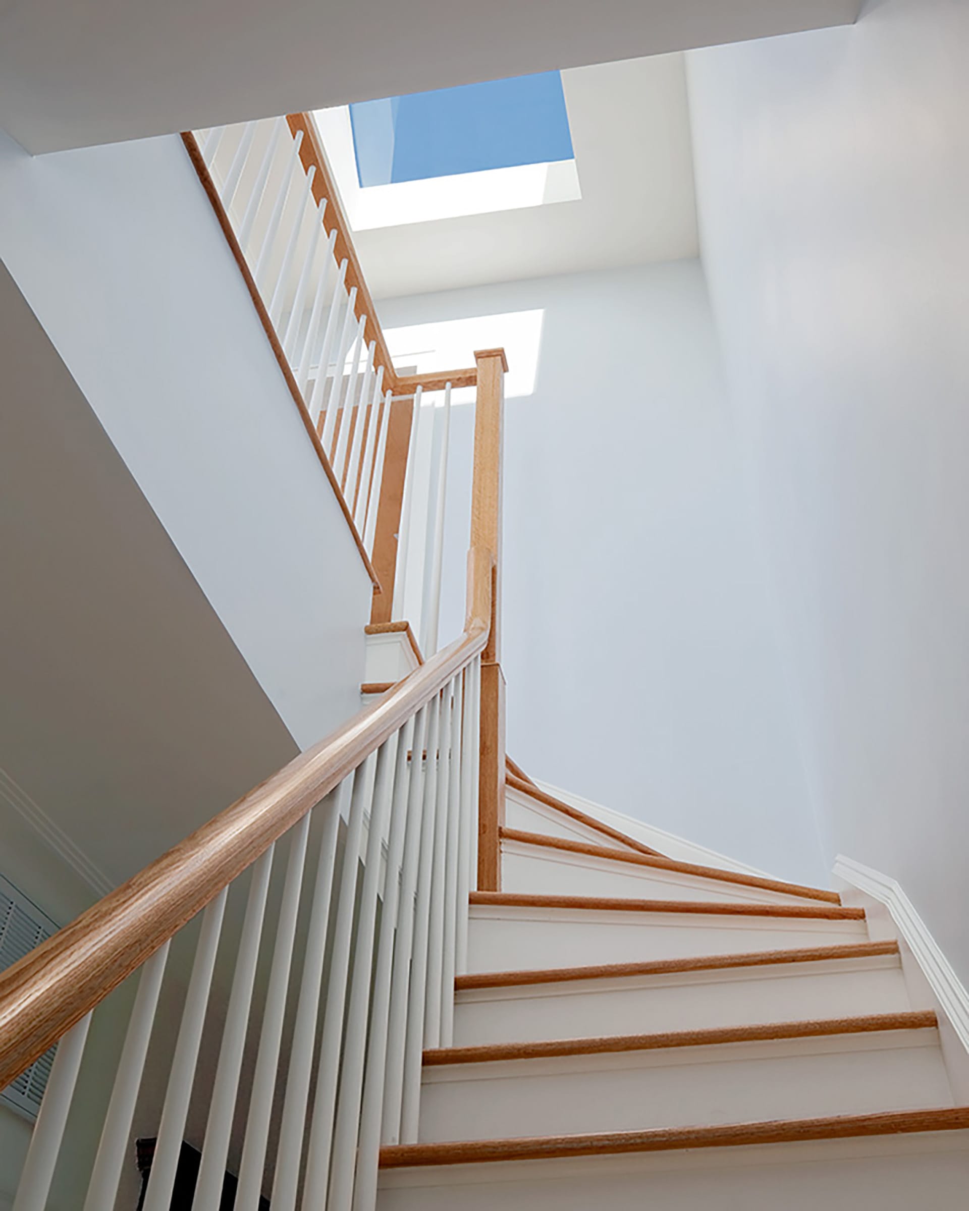 Staircase with natural wood handrail and a skylight above.