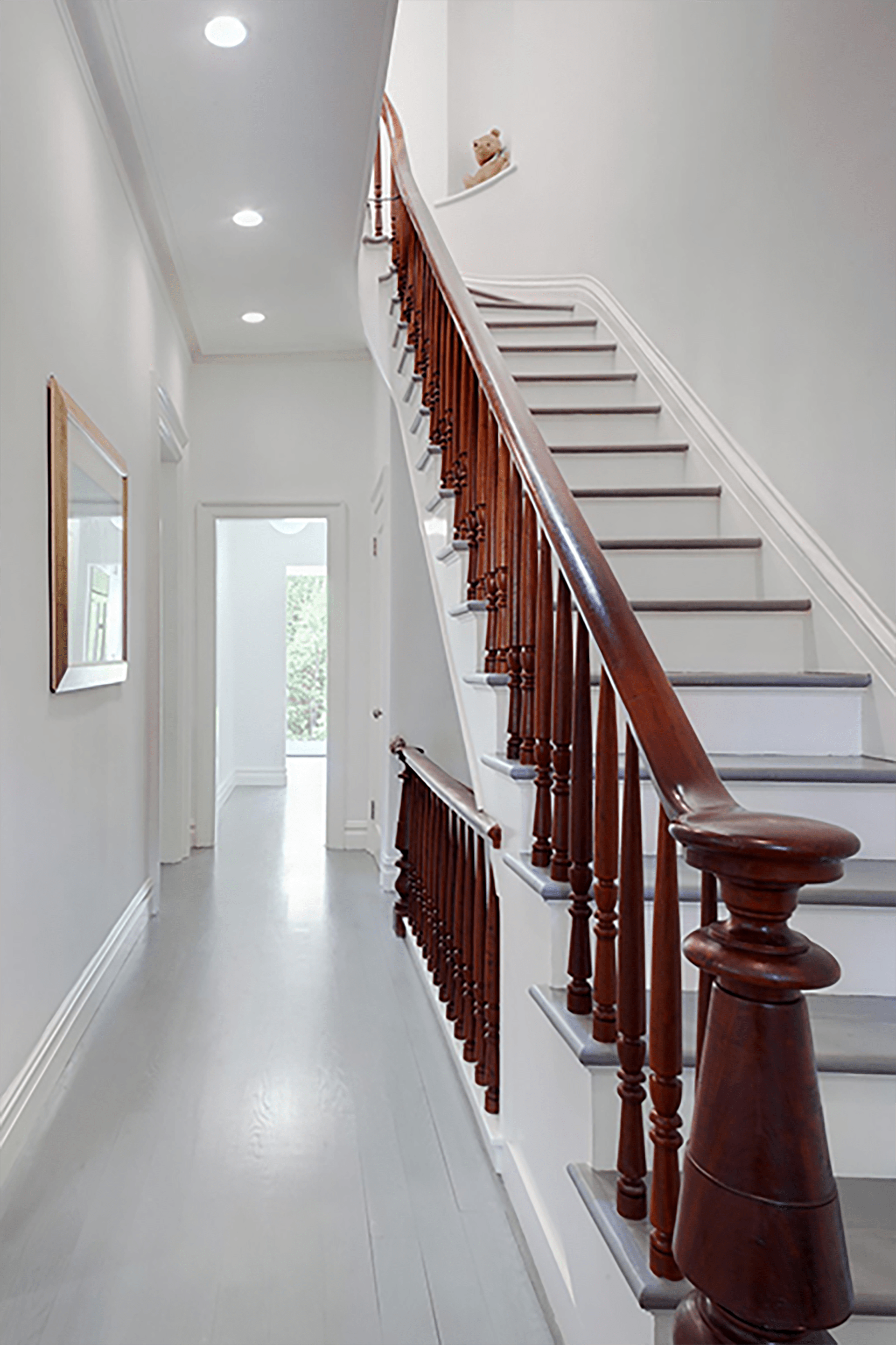 All white hallway with recessed lighting and staircase. The staircase has grey risers and the railings are mahogany.