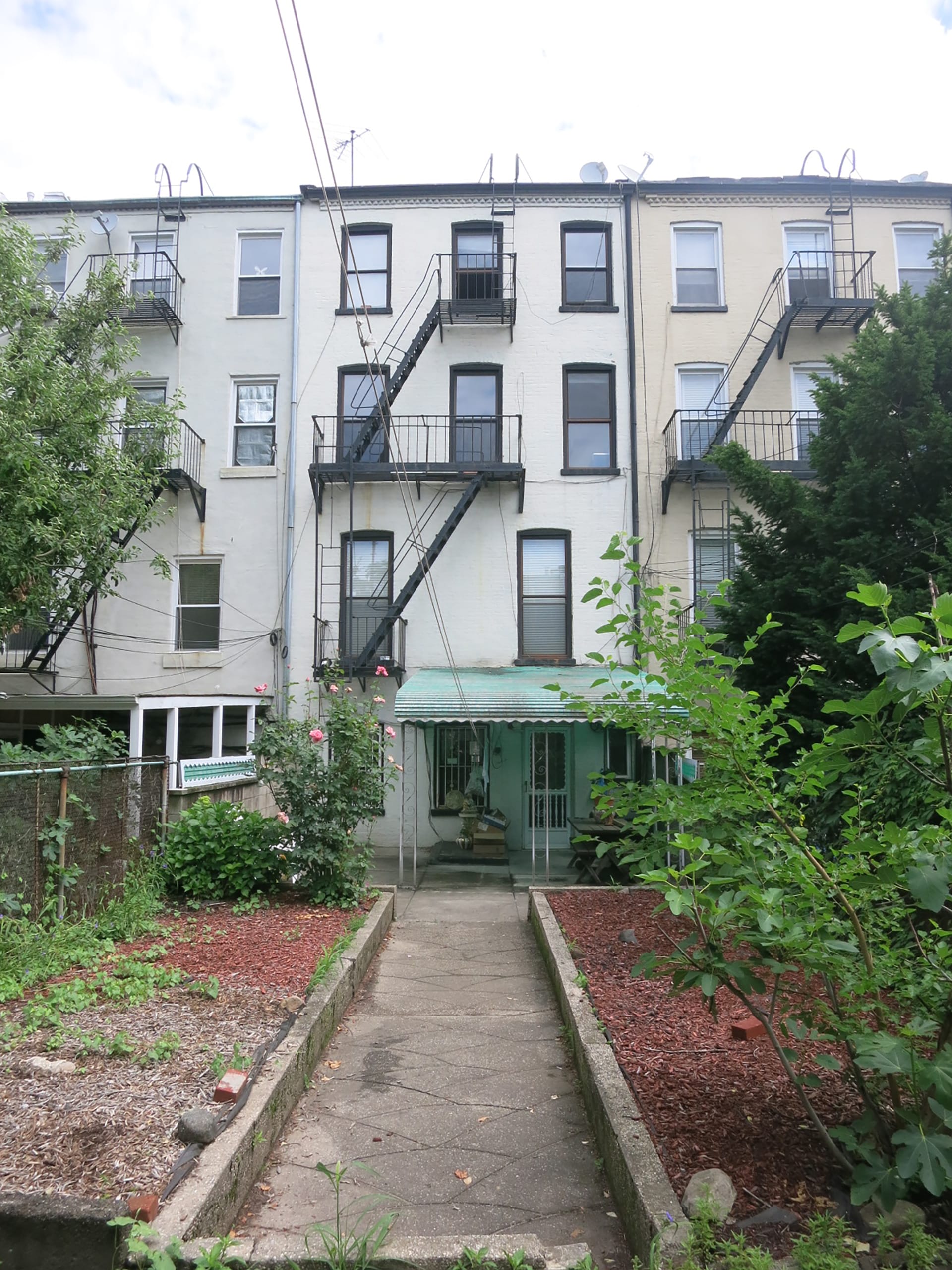 Rear façade of a brick townhouse with an awning on the first floor and white weatherproof coating on top of the brick