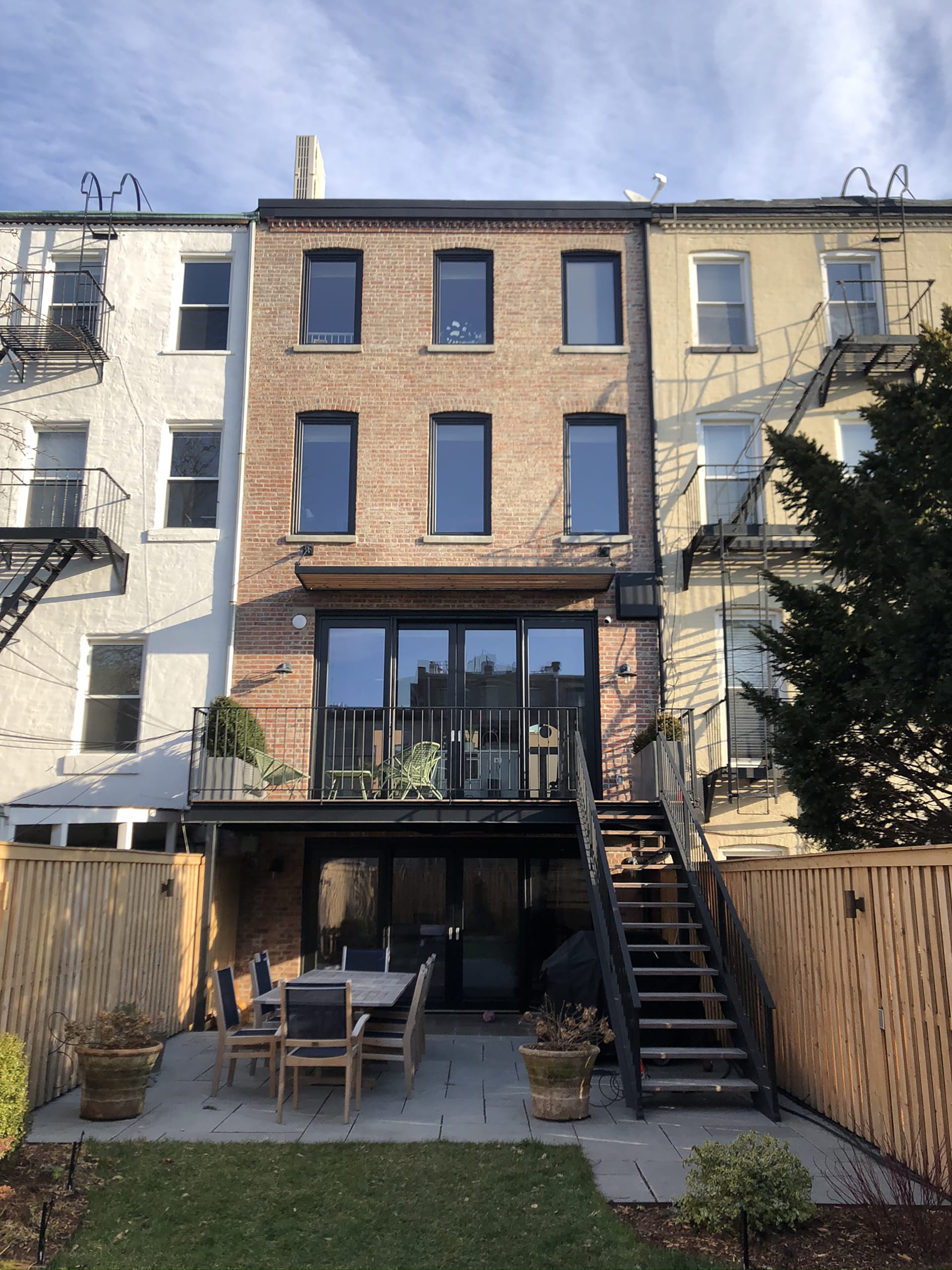 Rear façade of a Carroll Gardens townhouse with a new parlor-level deck, restored brick, and new larger windows and doors