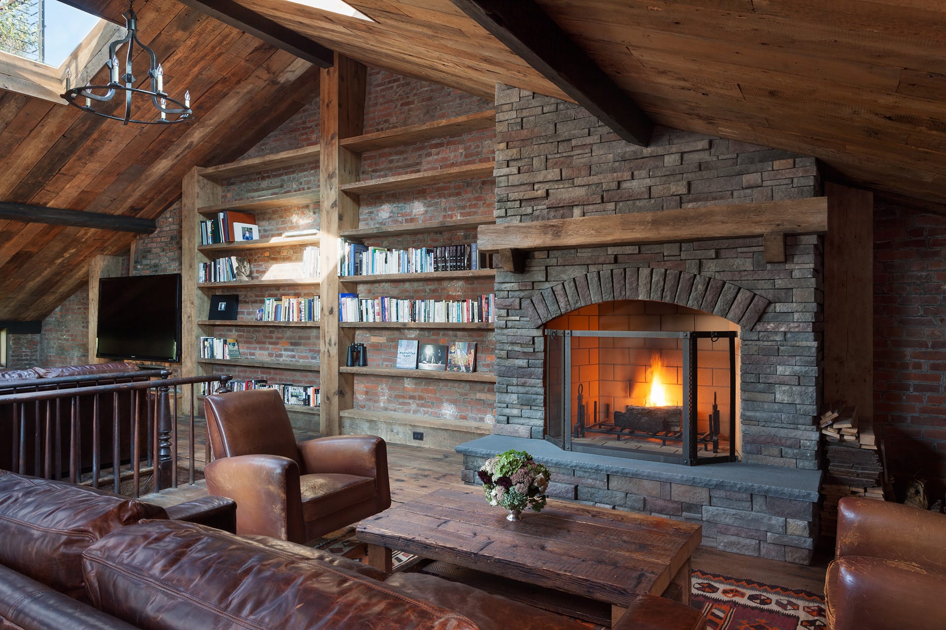 Attic of a Brooklyn Heights home with skylights, a wood-burning fireplace, wood paneled ceiling and exposed brick walls.