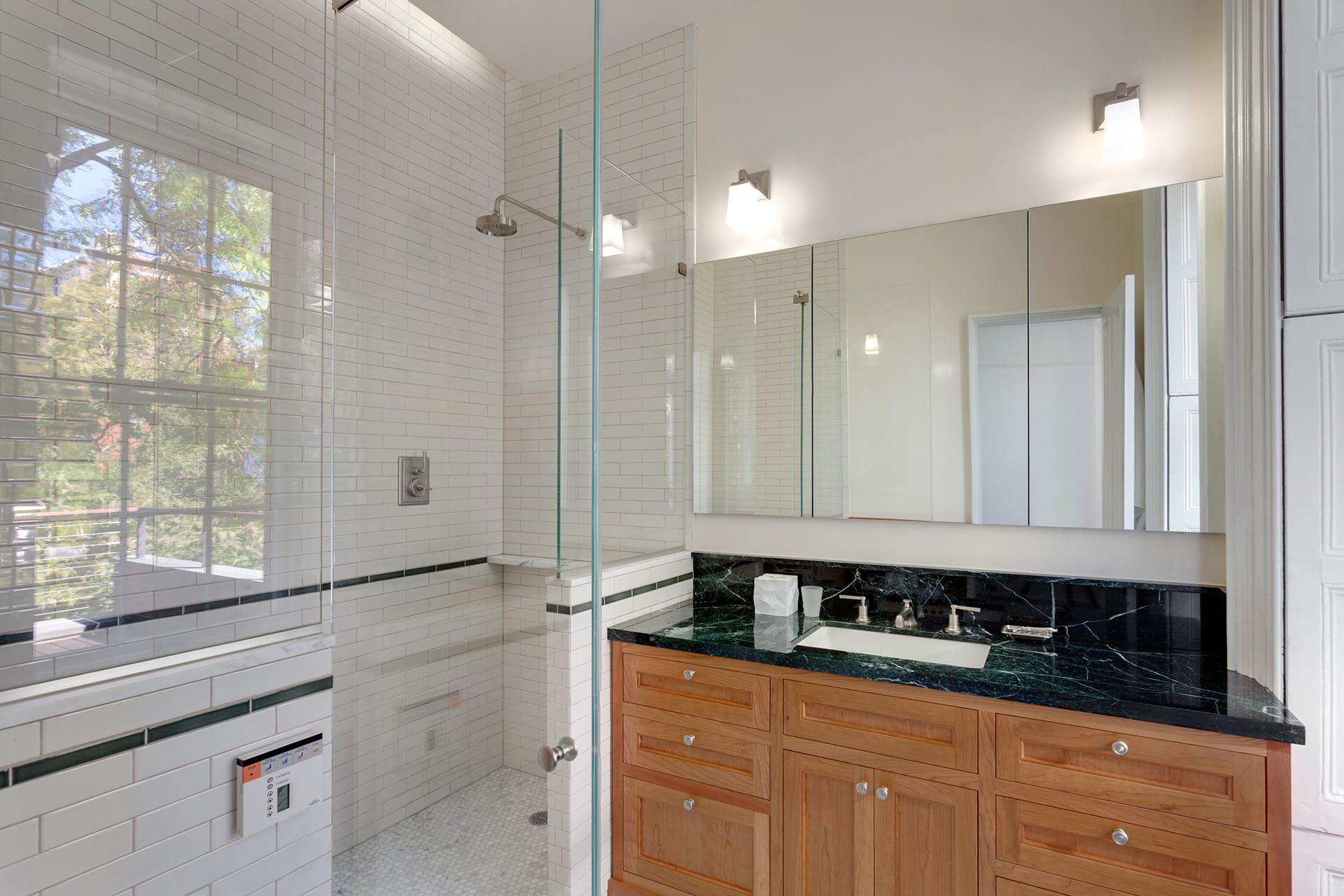 Shower stall of a primary bathroom with natural wood vanity and dark green marble countertop