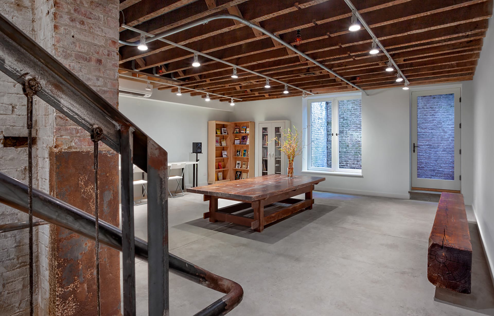 Gathering and research space with exposed beam ceilings, track lights, antique wood bench and table, and cement floors.