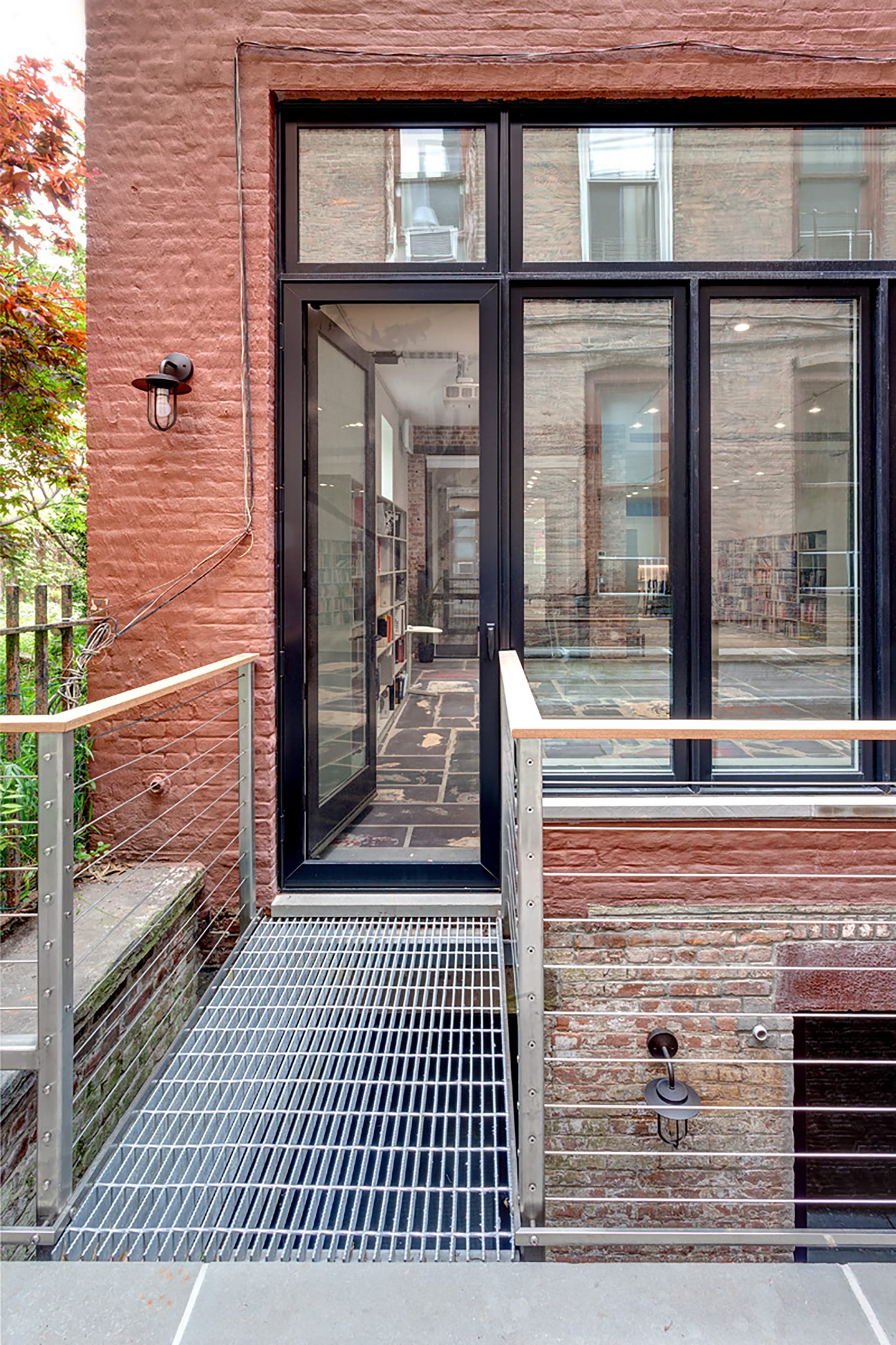 Metal bridge connecting a red brick building to a blue-stone paved rear yard over an areaway.