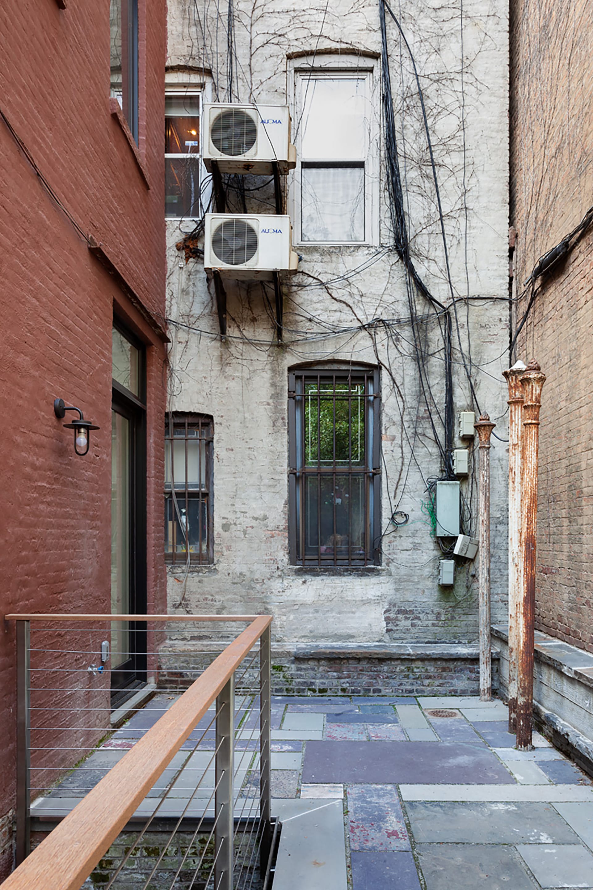 Bluestone patio in between a red brick building and a tan brick building with three salvaged cast iron poles.