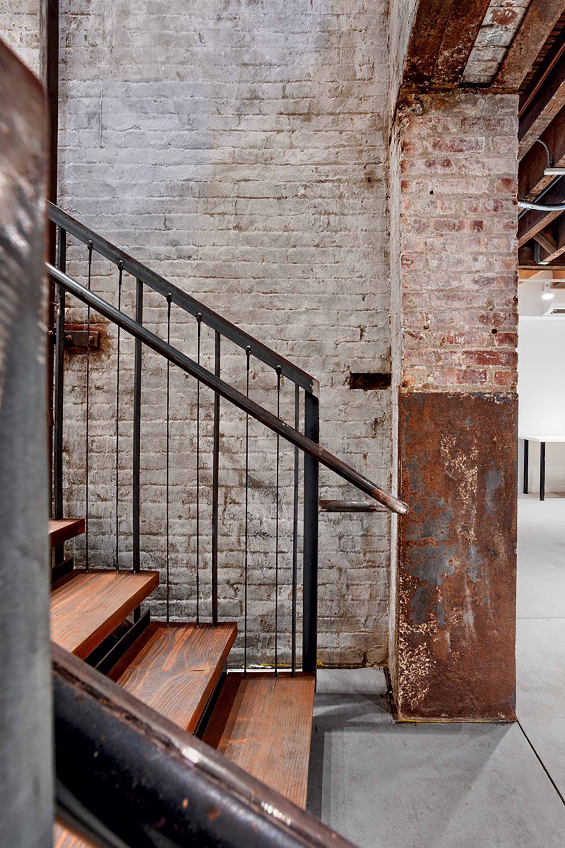 Stair landing with a wood-and-metal staircase in a converted elevator shaft with exposed brick