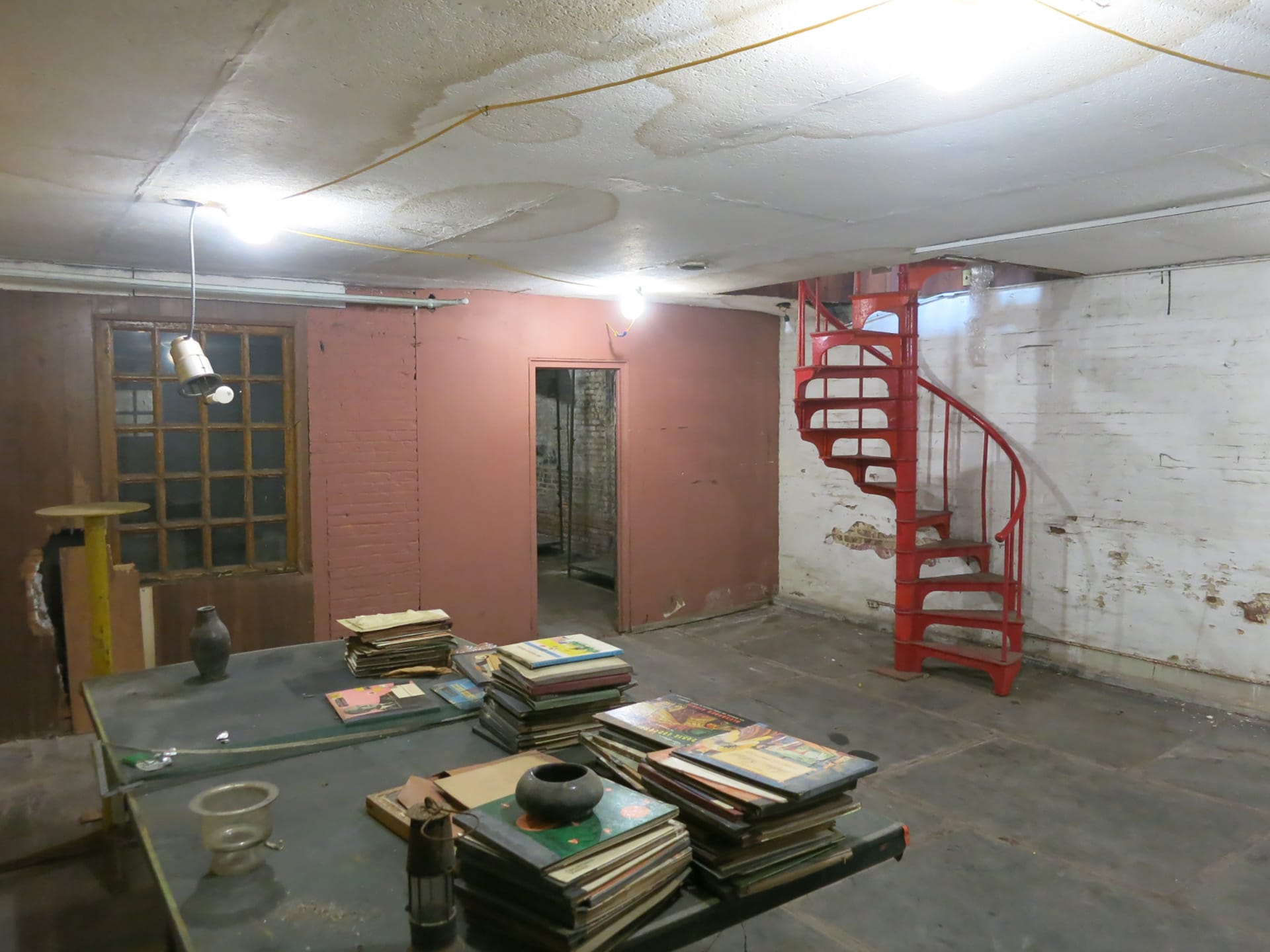 Red spiral staircase in a mostly empty room with painted exposed brick walls.