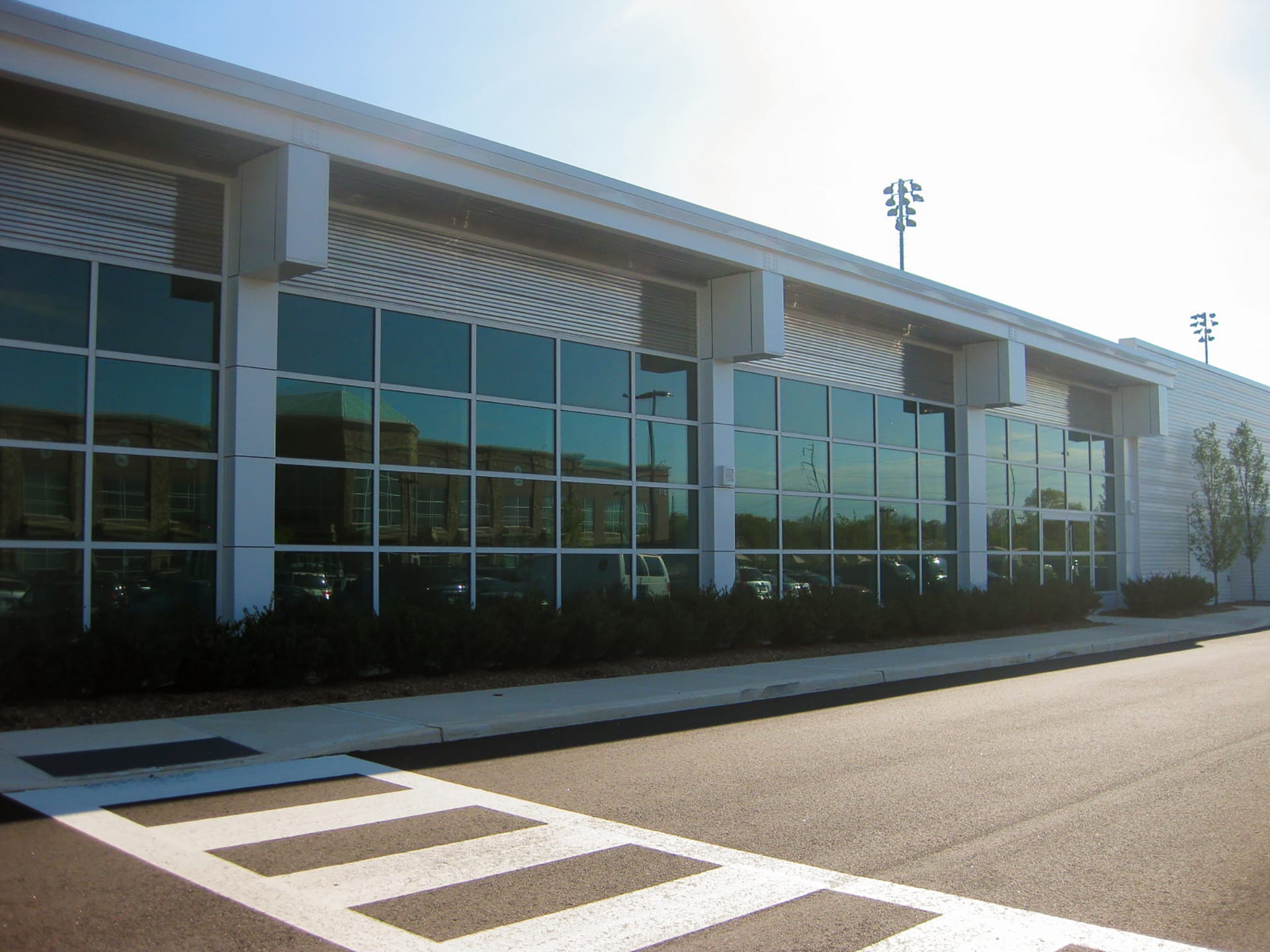 Exterior of a bicycle shop, with a parking lot, large expanses of glass, and bushes in front of the building.