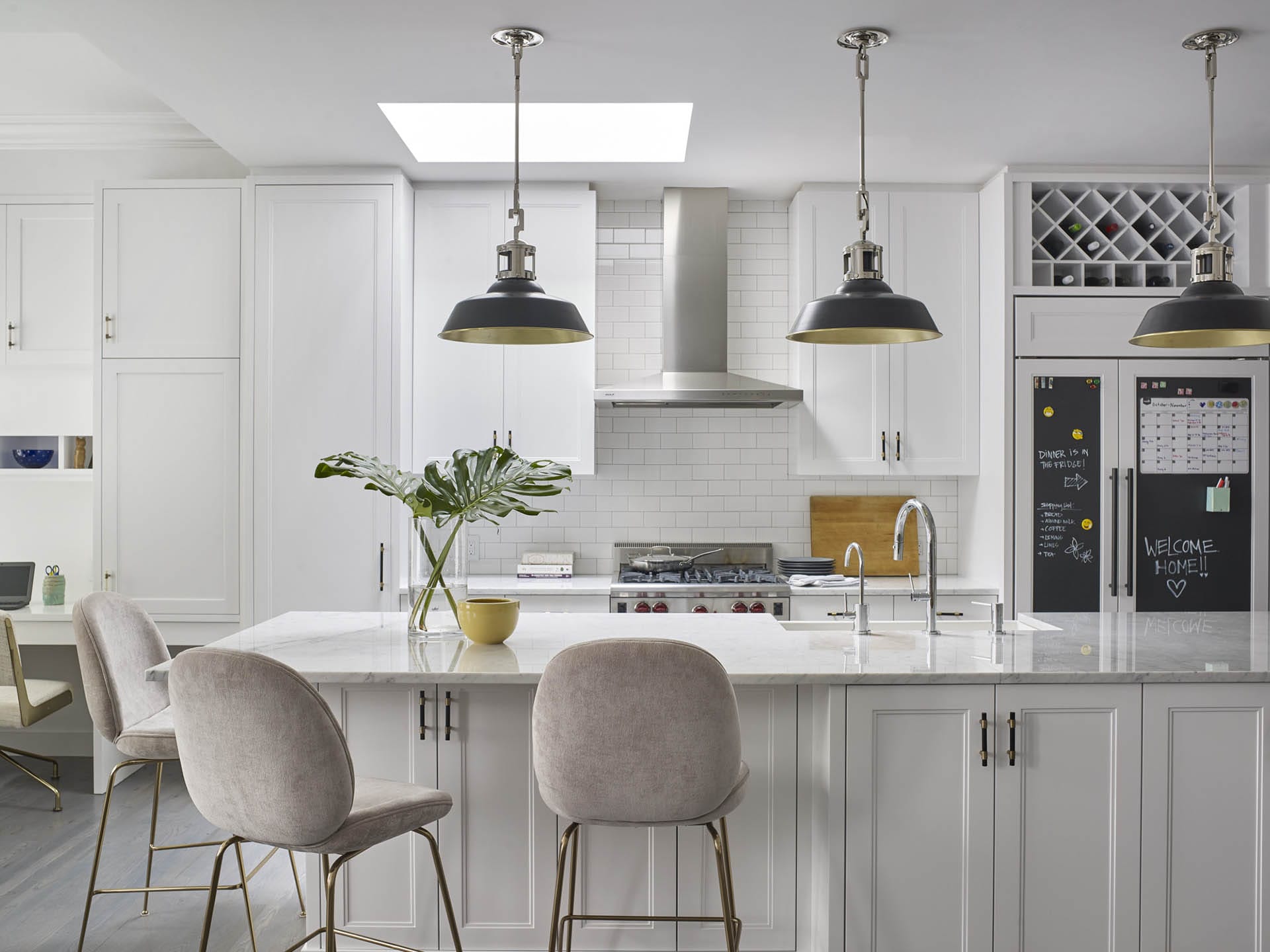 Open, all-white kitchen with black pendant lights hanging above the kitchen island