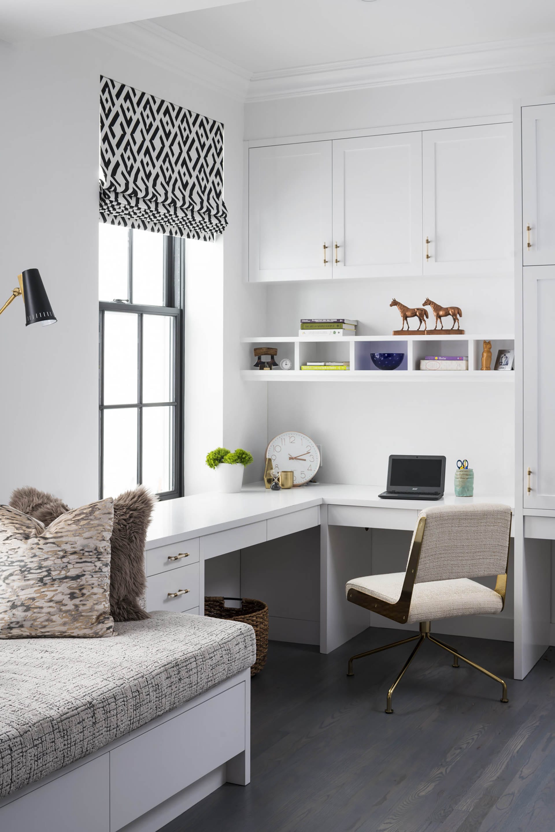 Corner office space next to the kitchen with black and white Roman shades and white built-in desk, cabinets, and shelves.