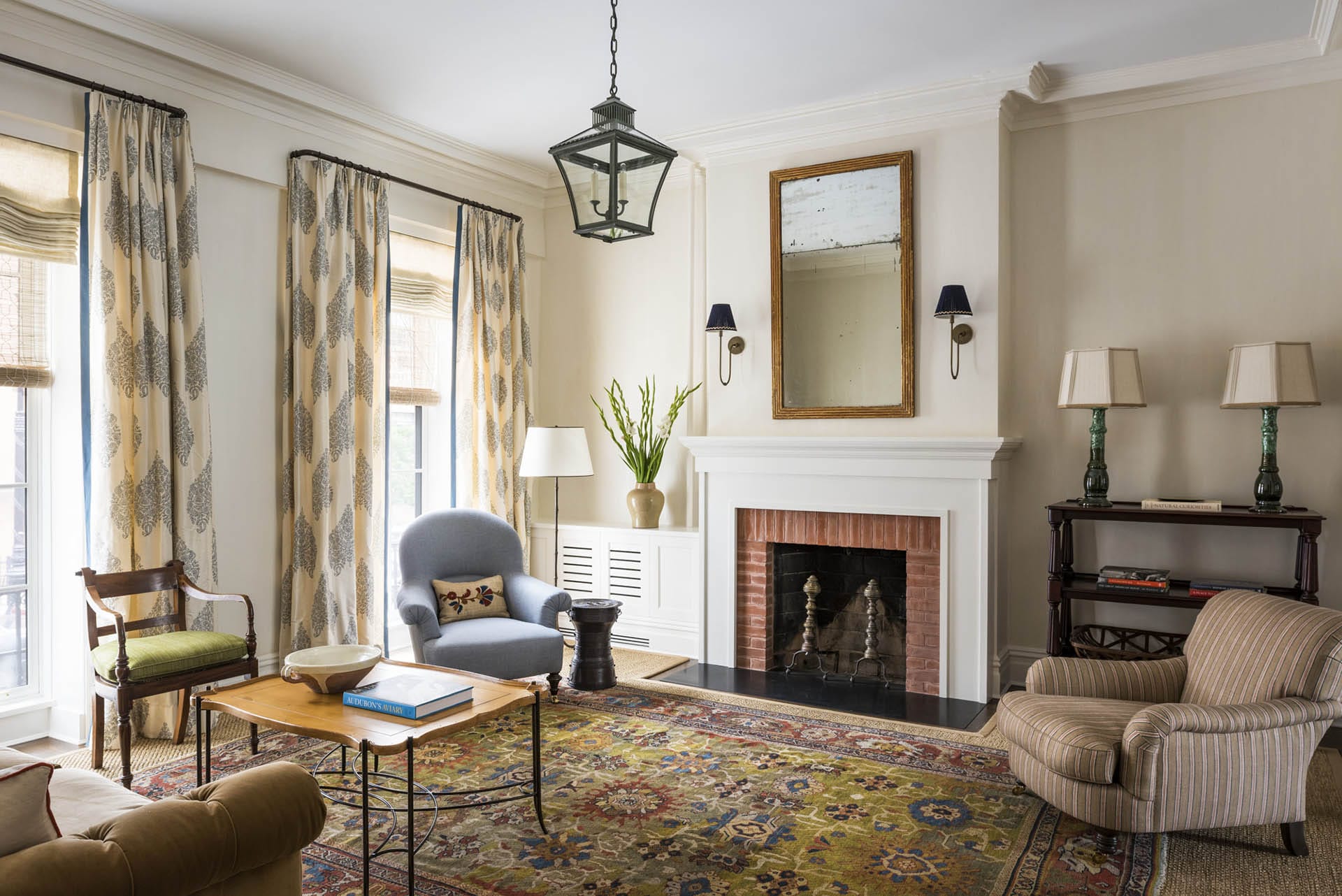 Traditional living room with mismatched chairs, a large rug, and leaf-printed curtains.