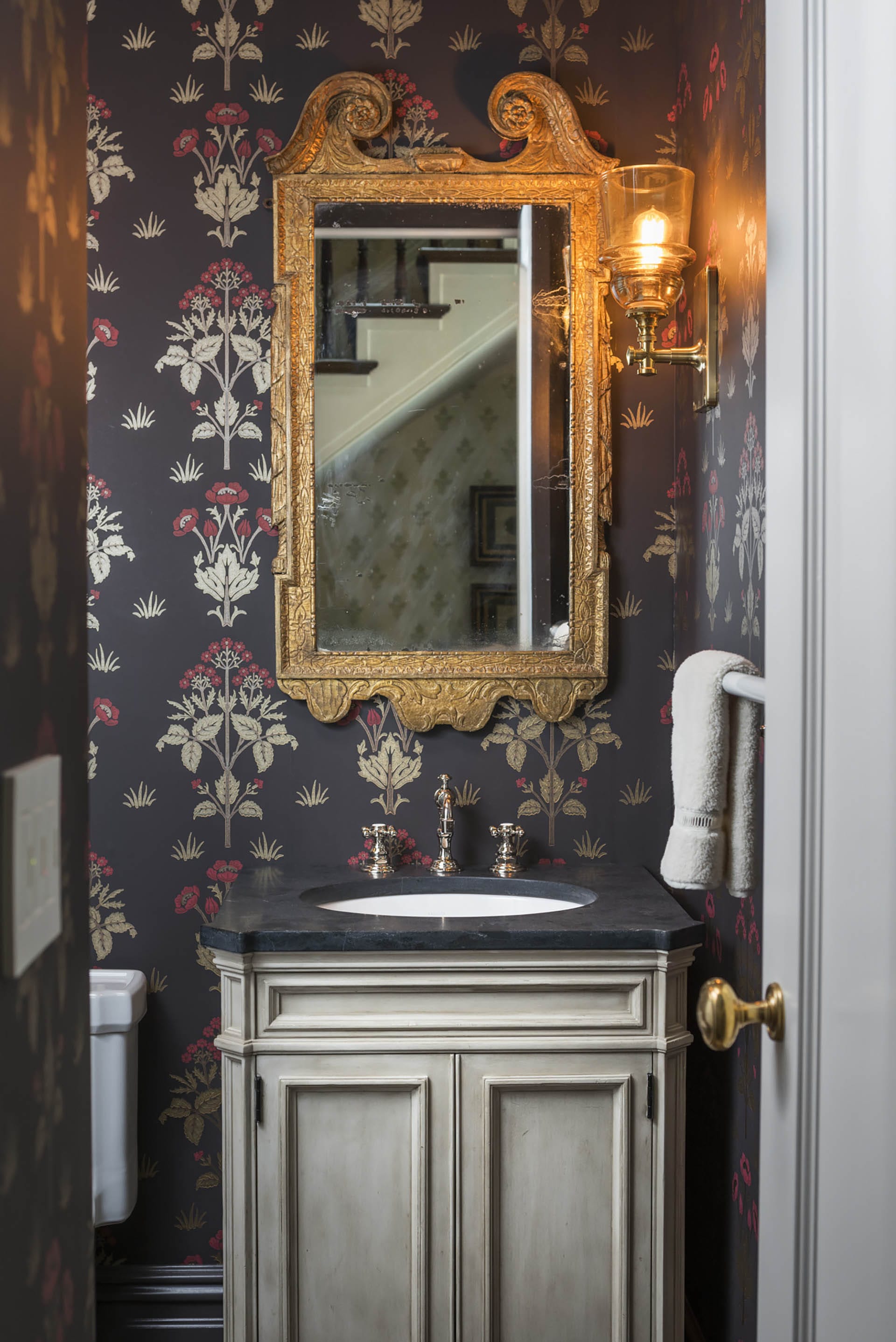 Powder room with an ornate gold mirror, purple floral wallpaper,, and a wall sconce