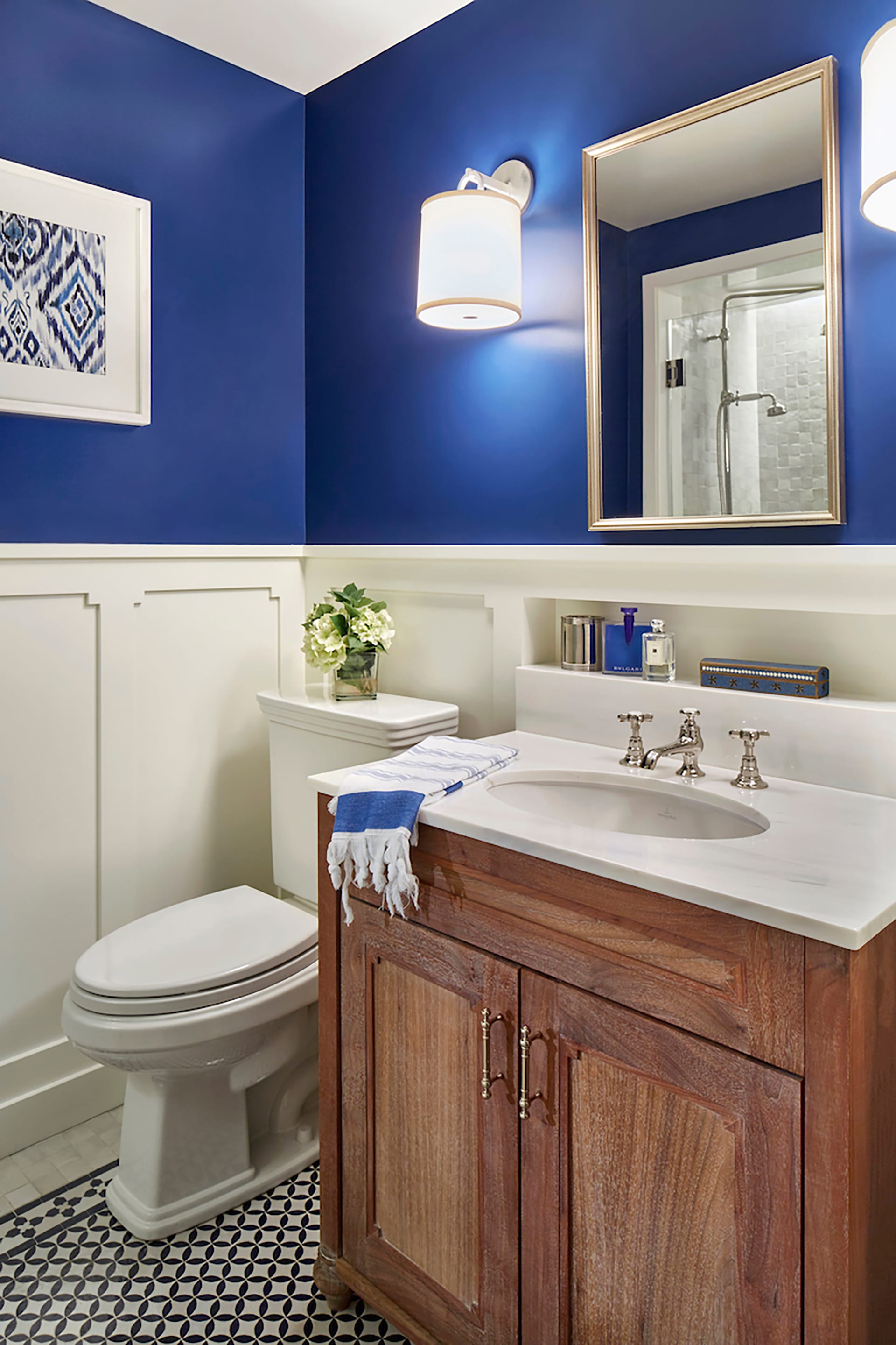 Guest bathroom with polished nickel fixtures, royal blue paint on the top half, and white paneling on the bottom half of the walls.