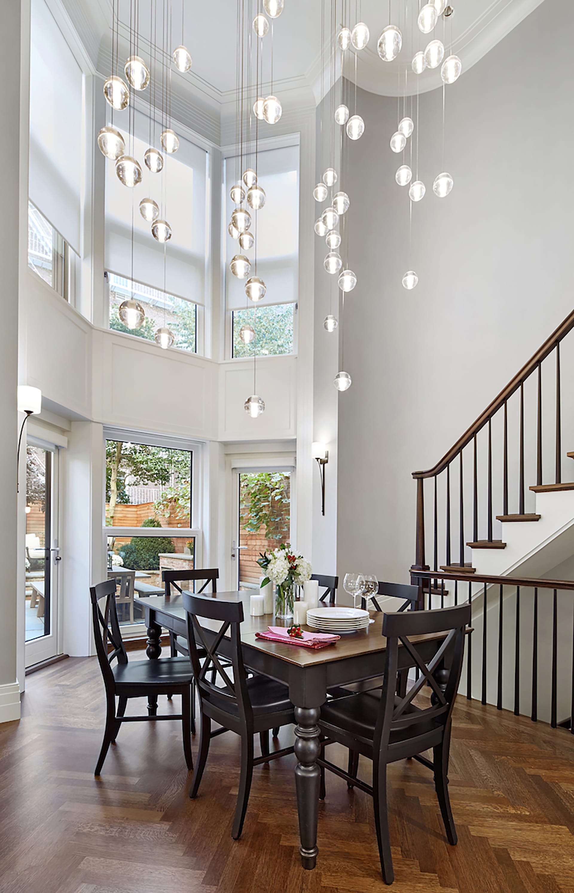 Dining area in a double height space with a two-story bay window and a hanging Bocce light fixture installation