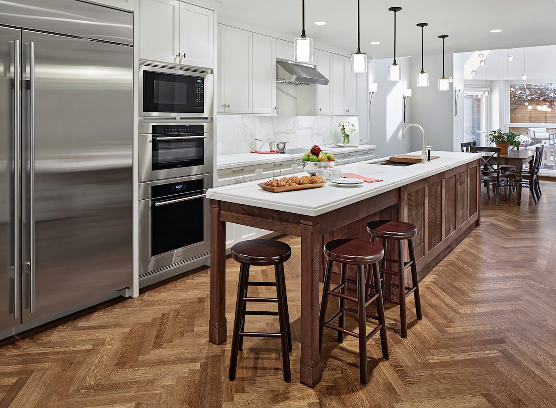 Kitchen with herringbone wood floors, pendant lights above the island, and white cabinetry.