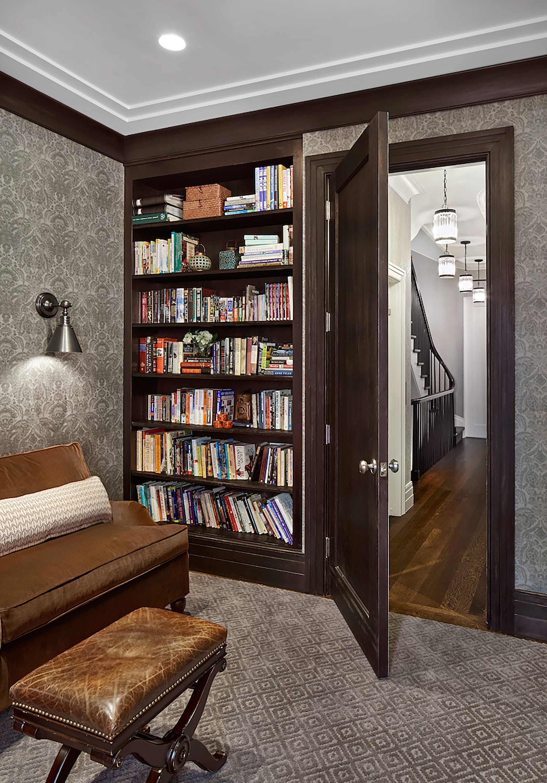 Library with grey patterned wallpaper, dark wood door and accents, and built-in bookshelves.