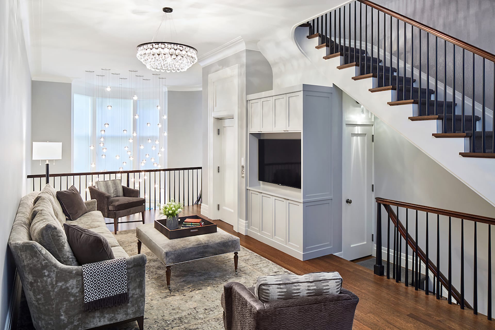 Living room with shaker-style millwork, grey velvet furniture, and a large chandelier overlooking a double height space