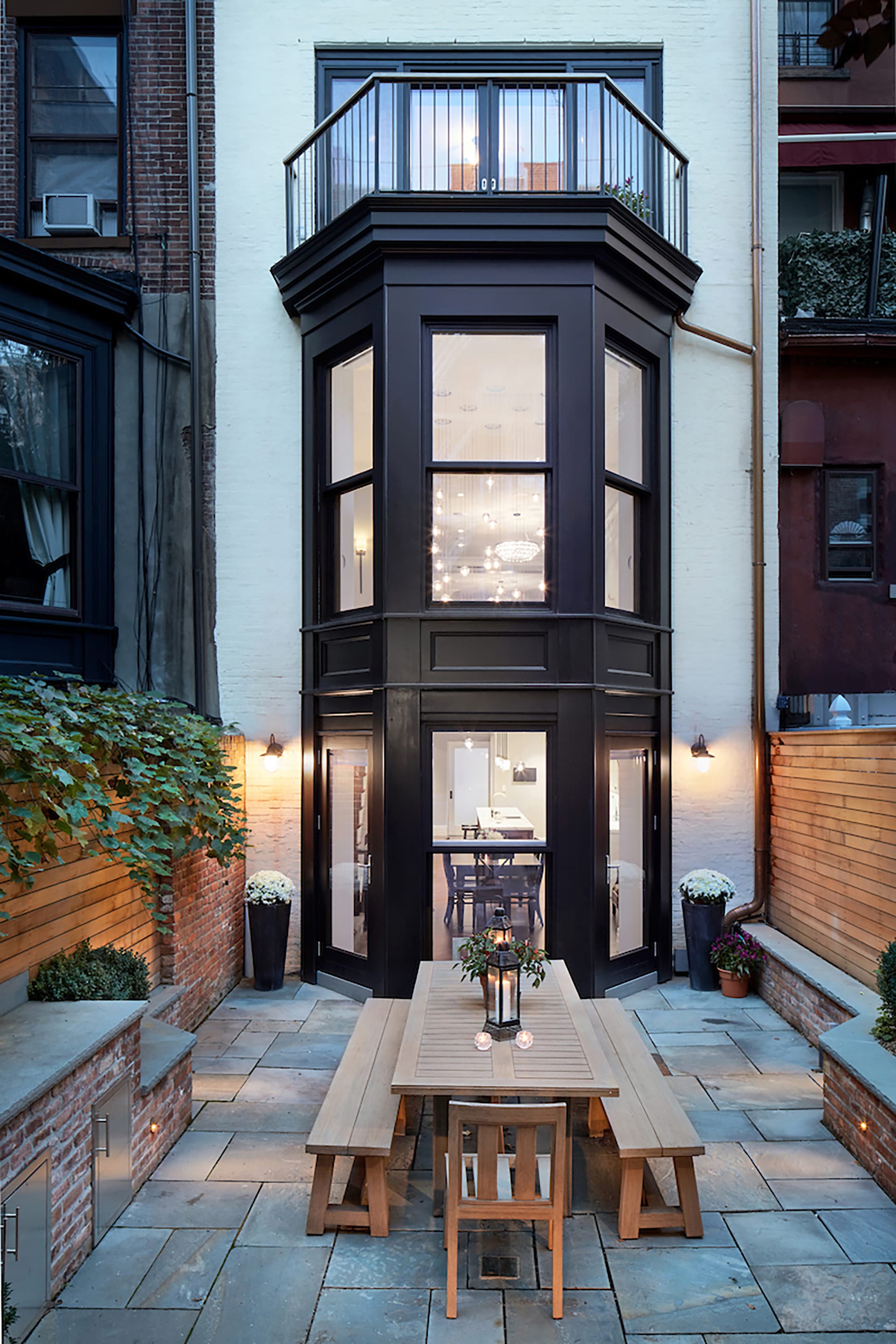 White painted brick rear facade with a two-story black bay window and balcony atop it after our renovation