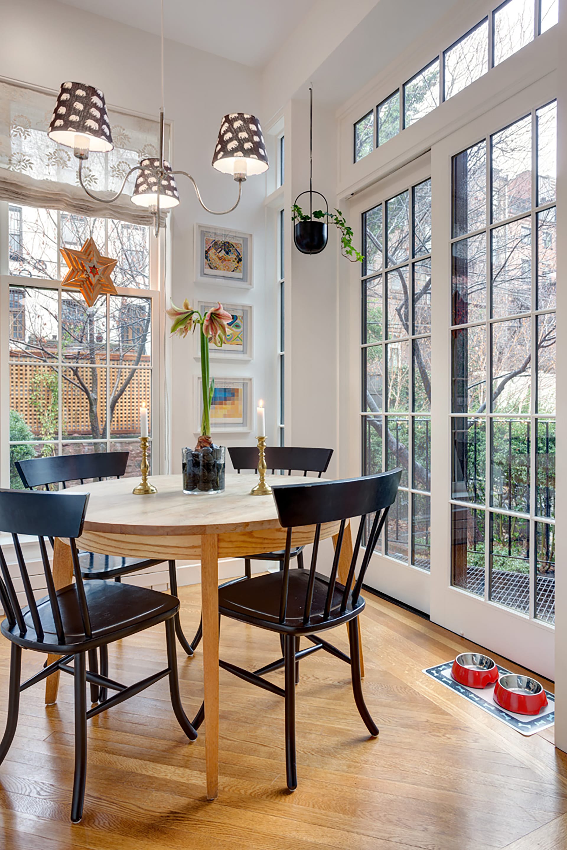 Informal dining area with newly restored wood floors and windows, wood circular table with black chairs, leading out to the rear yard of a Brooklyn Heights home