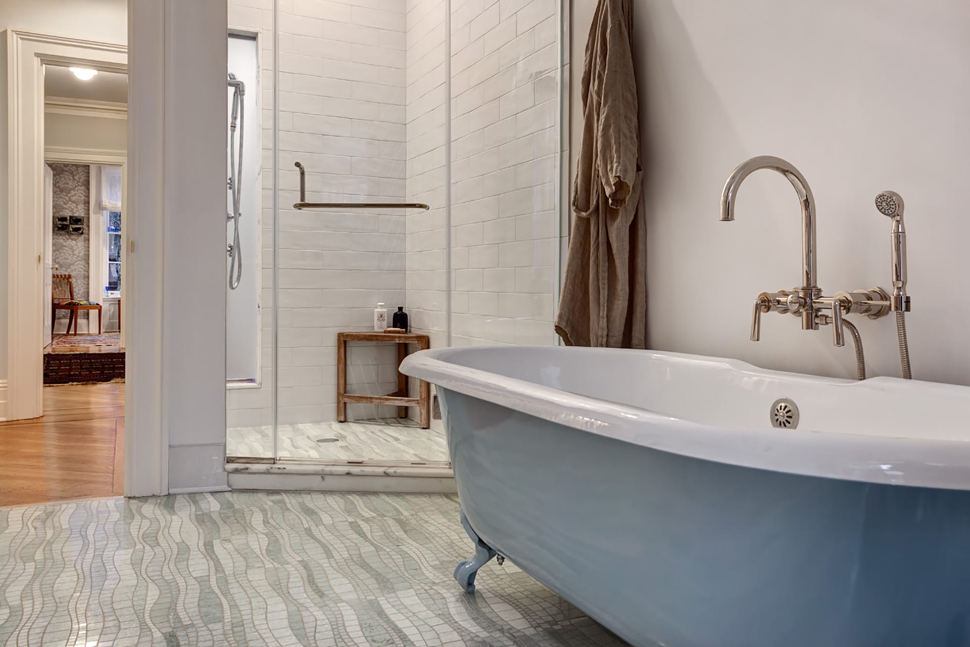 Blue clawfoot tub in the foreground of a primary bathroom with tiled floors and a shower stall.