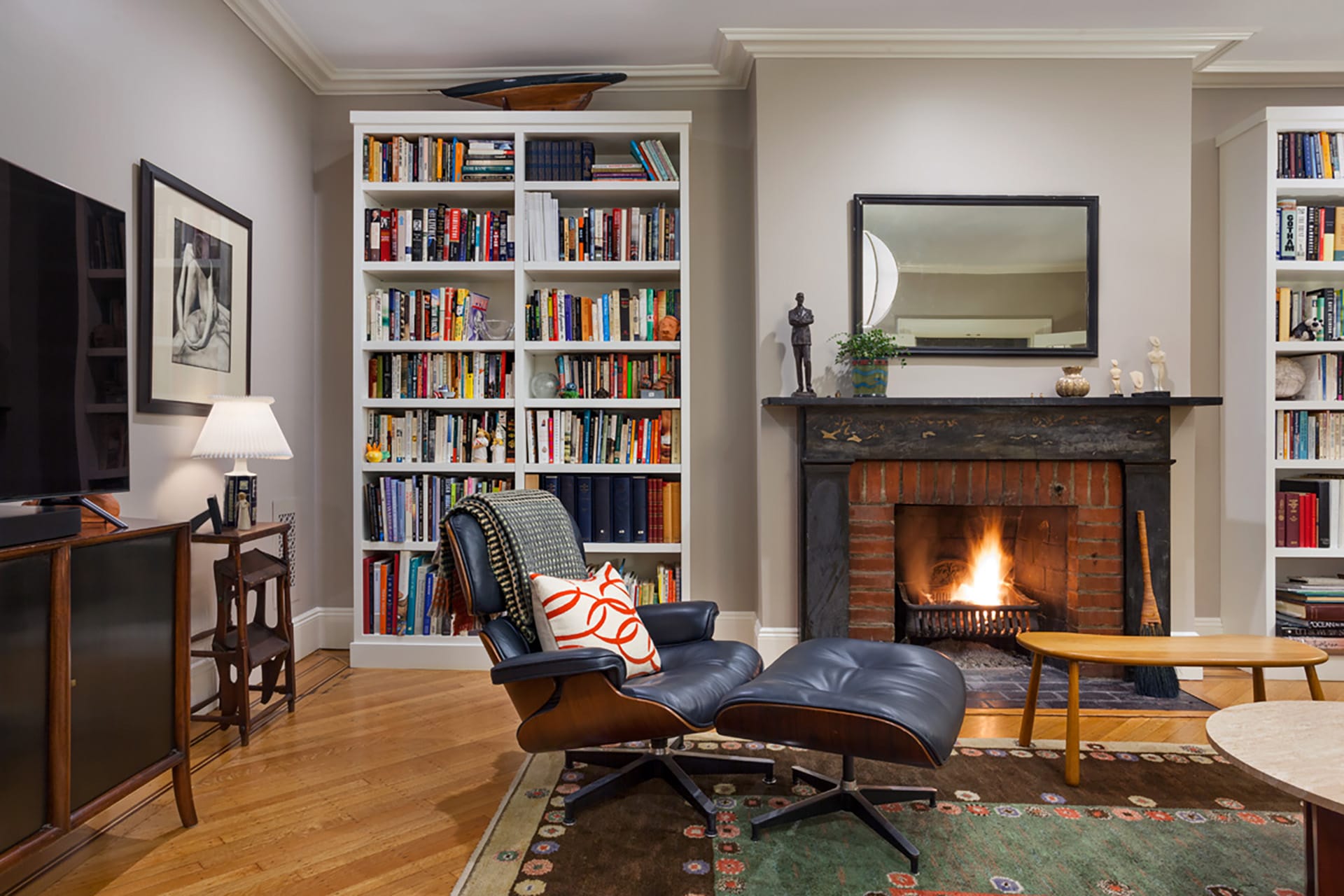 Formal study with wood floors, a fireplace, large white bookshelves, and a black and wood lounge chair in a Brooklyn Heights home