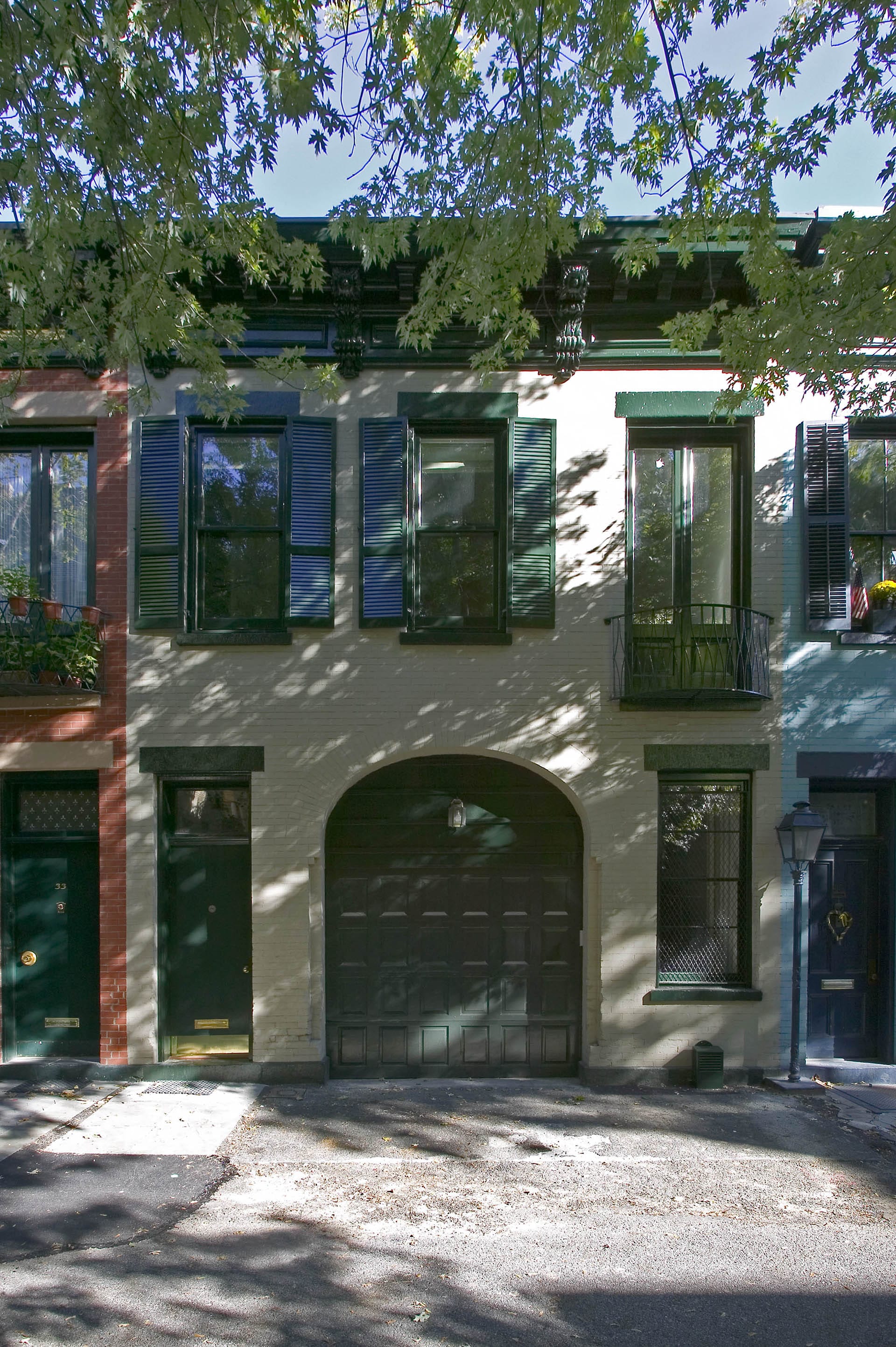 Front facade of a carriage house with white painted brick and dark green shutters, lintels, and doors.