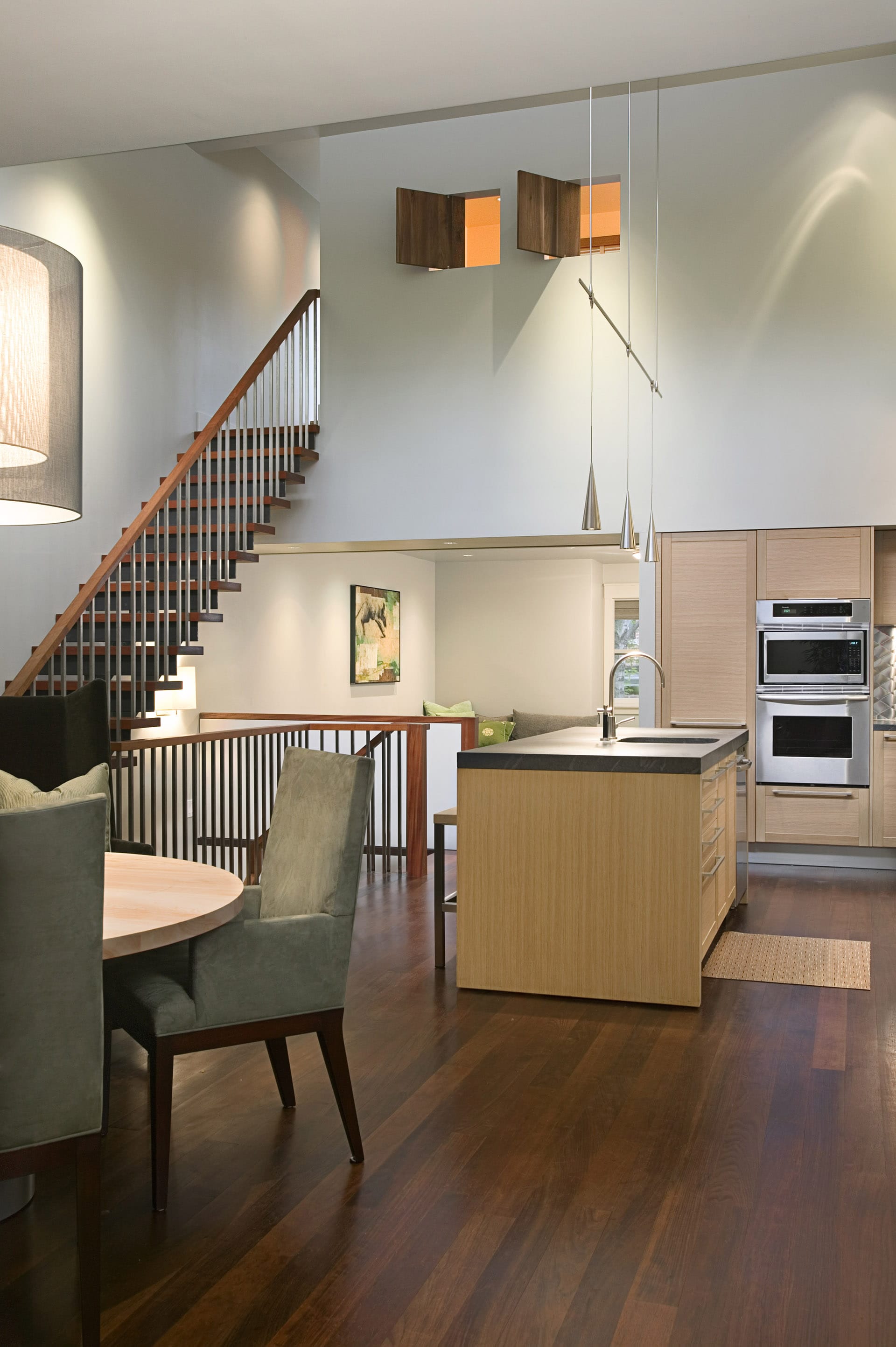 Modern double-height kitchen with dark wood floors, light wood cabinetry and island, and stainless steel backsplash and appliances.