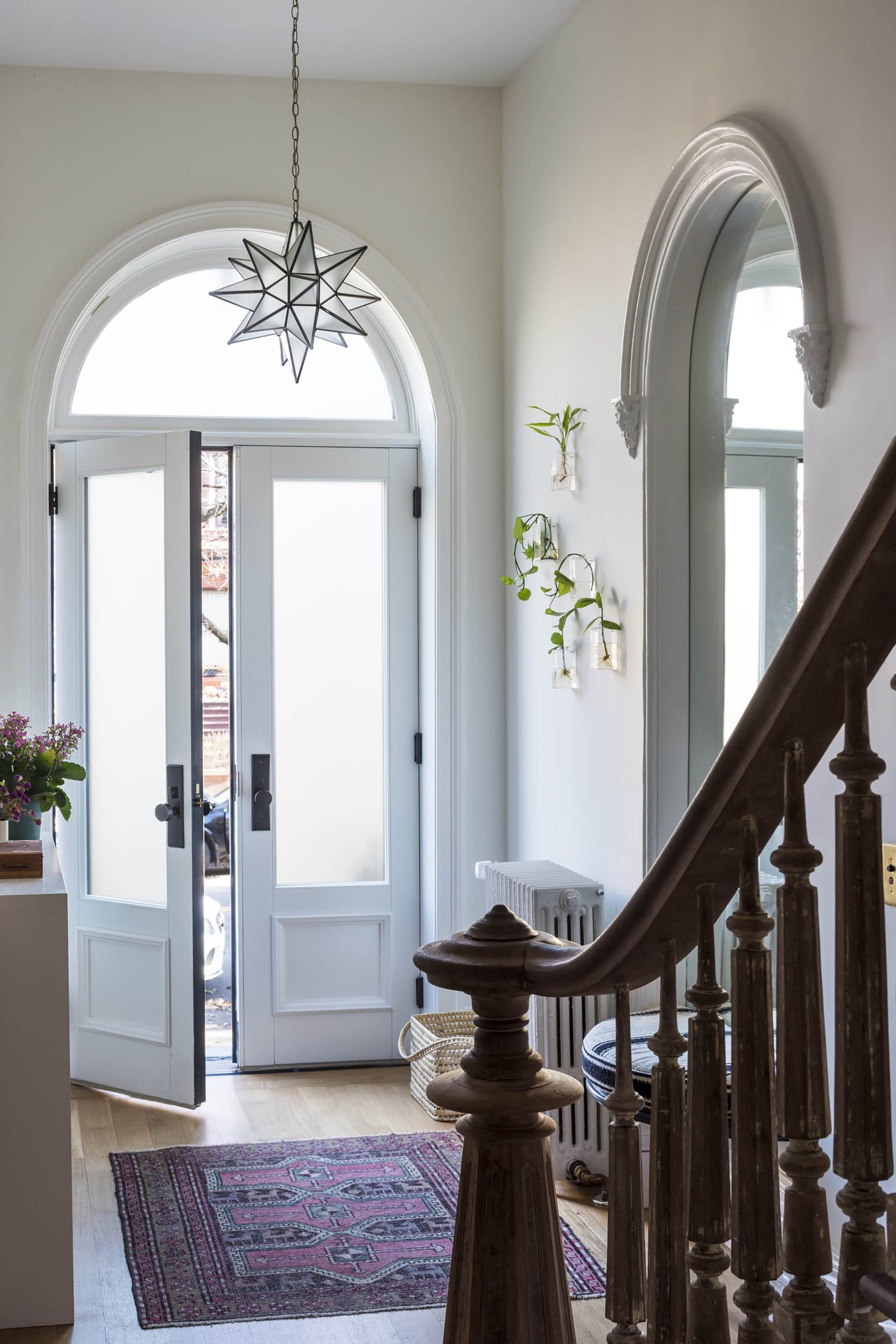 Entryway of a Clinton Hill rowhome with recreated historic doors and transom, geometric light fixture, and historic newel and railing in the foreground.