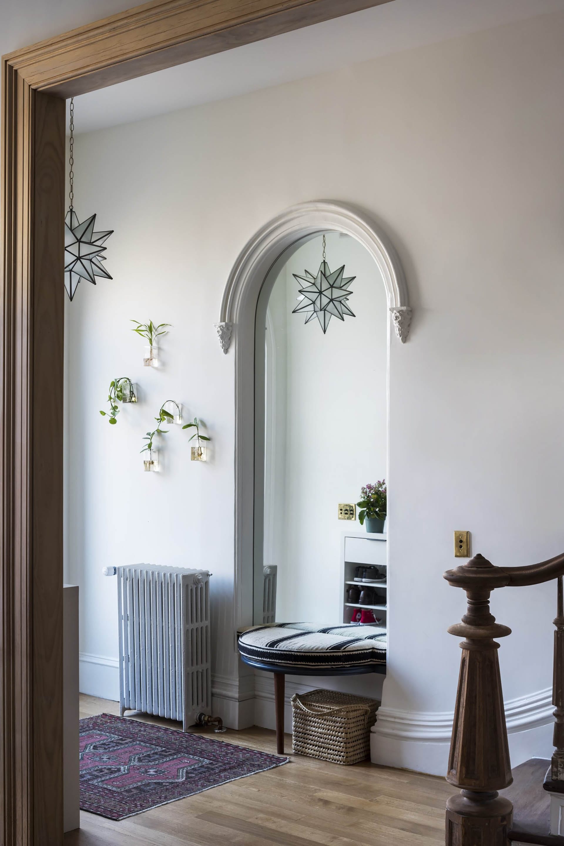 Entryway of a Clinton Hill rowhome with arched mirror, geometric light fixture, and historic newel and railing in the foreground.