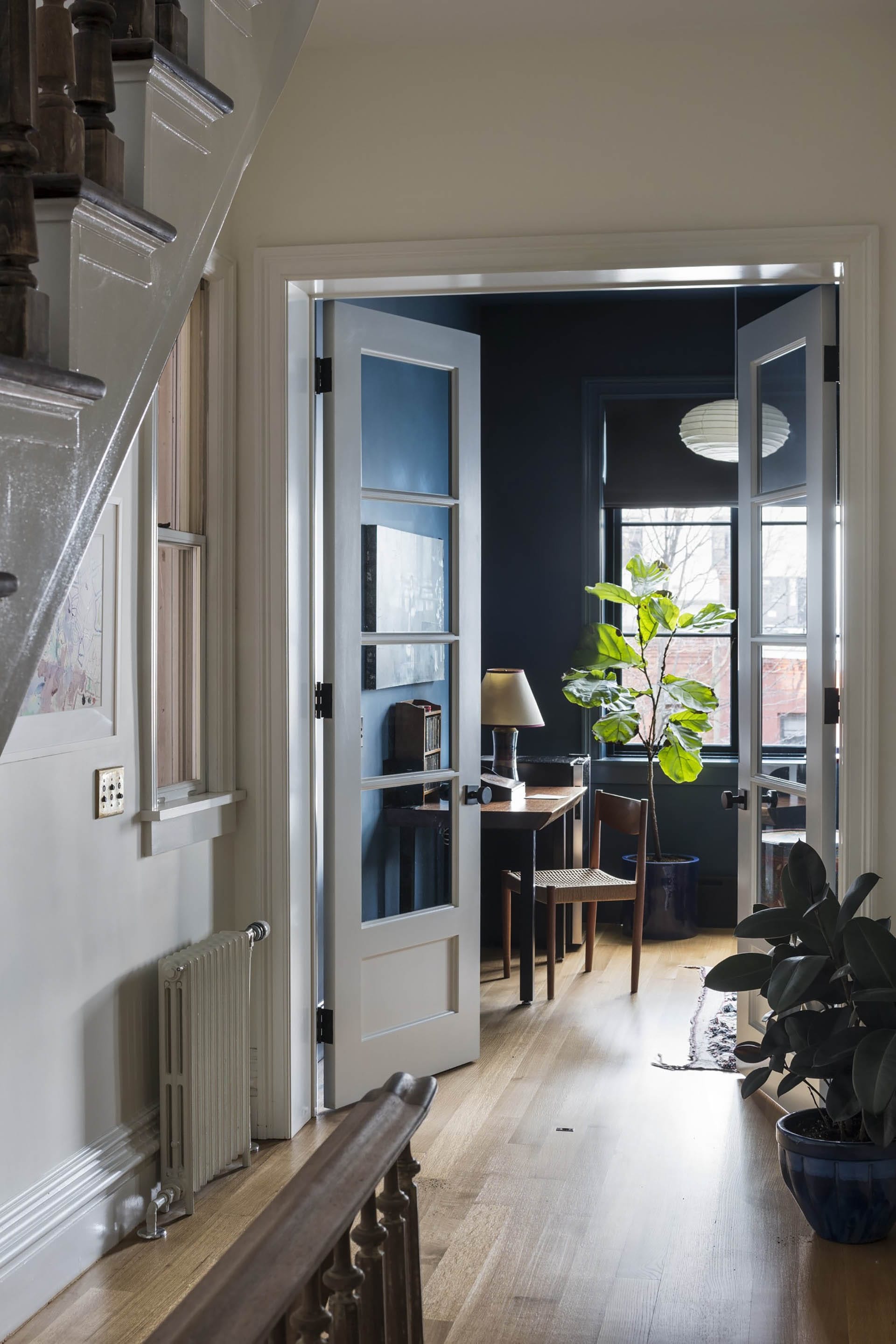 Hallway in a Clinton Hill rowhome with light wood floors and glazed French doors leading into a dark teal room.