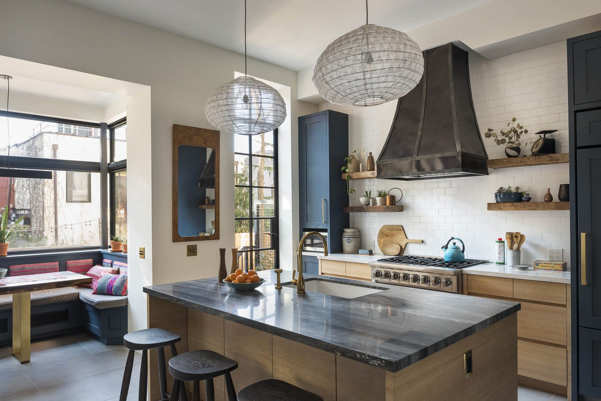 Kitchen with natural wood island, dark teal floor-to-ceiling cabinets, subway tile, marble countertops and a breakfast nook.