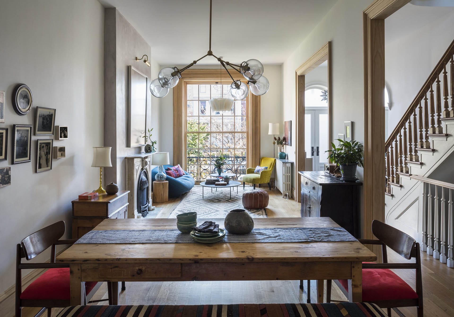 Open concept parlor floor of a Clinton Hill rowhouse with a natural wood dining table, living room area, and historic fireplace.