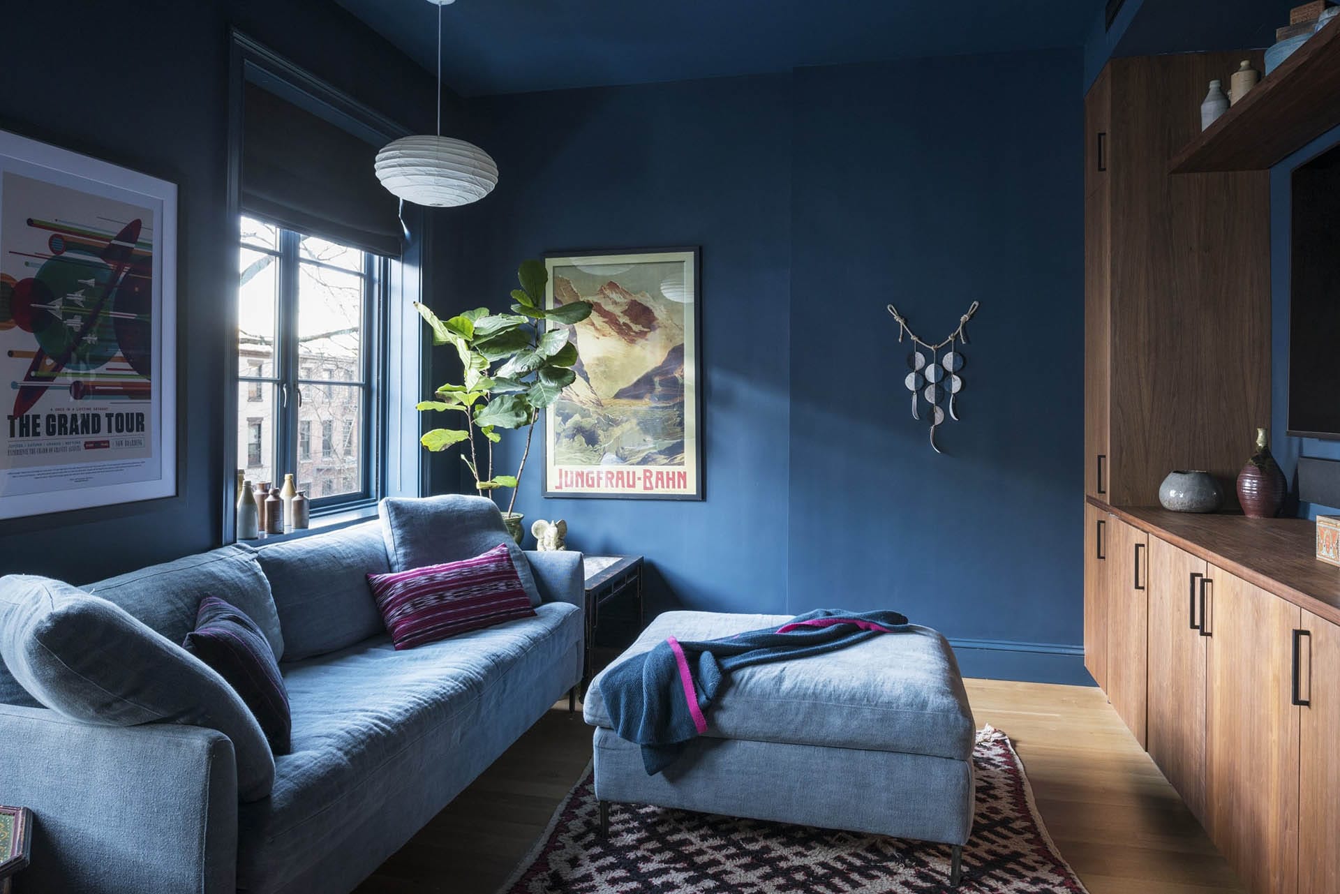 Dark teal painted TV room with a grey couch and custom, natural wood cabinetry.