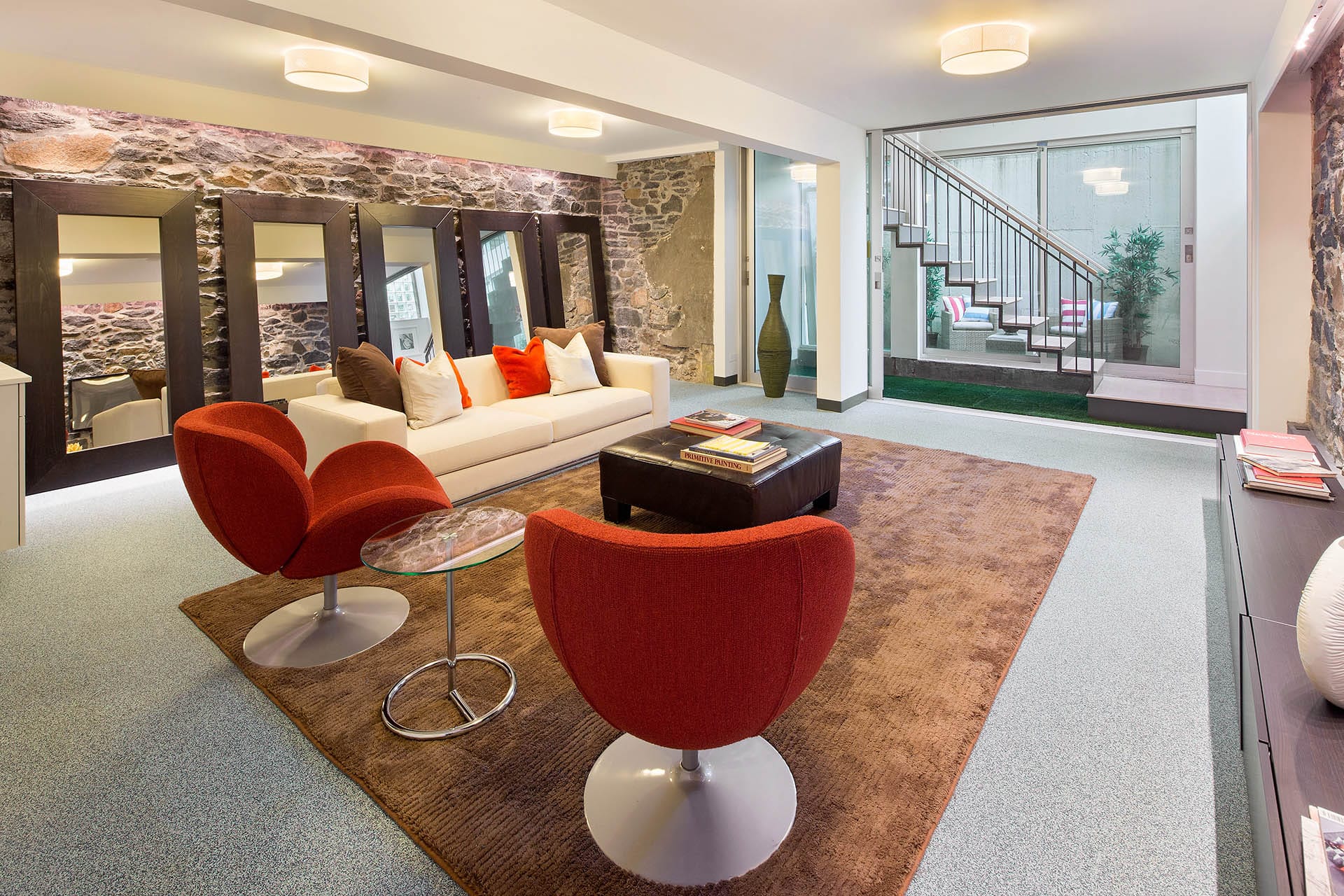 Entertainment space in the cellar of a Cobble Hill carriage house with exposed fieldstone walls and a glass wall showcasing a below-grade outdoor seating area.