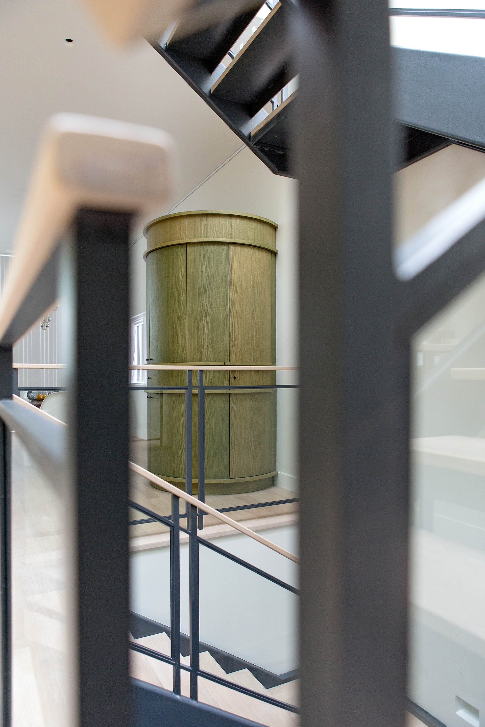 View of an artisan-crafted round, green pantry from a modern metal staircase.