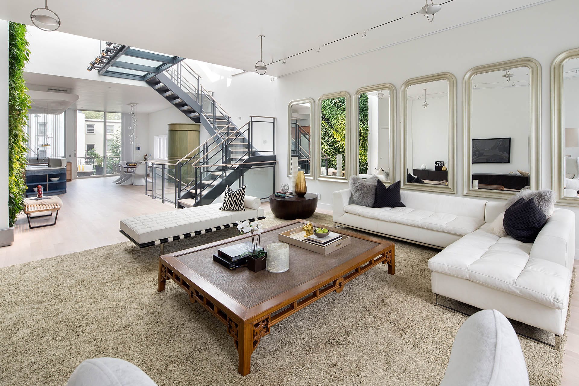 Neutral living room with white furniture and 5 large mirrors on the wall. The space opens to a living wall and the kitchen.