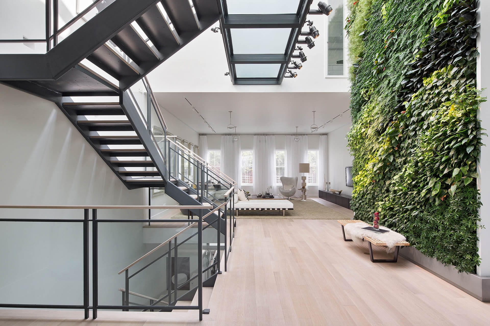 Open concept floating staircase leading to a rear living room with a wall of plants.