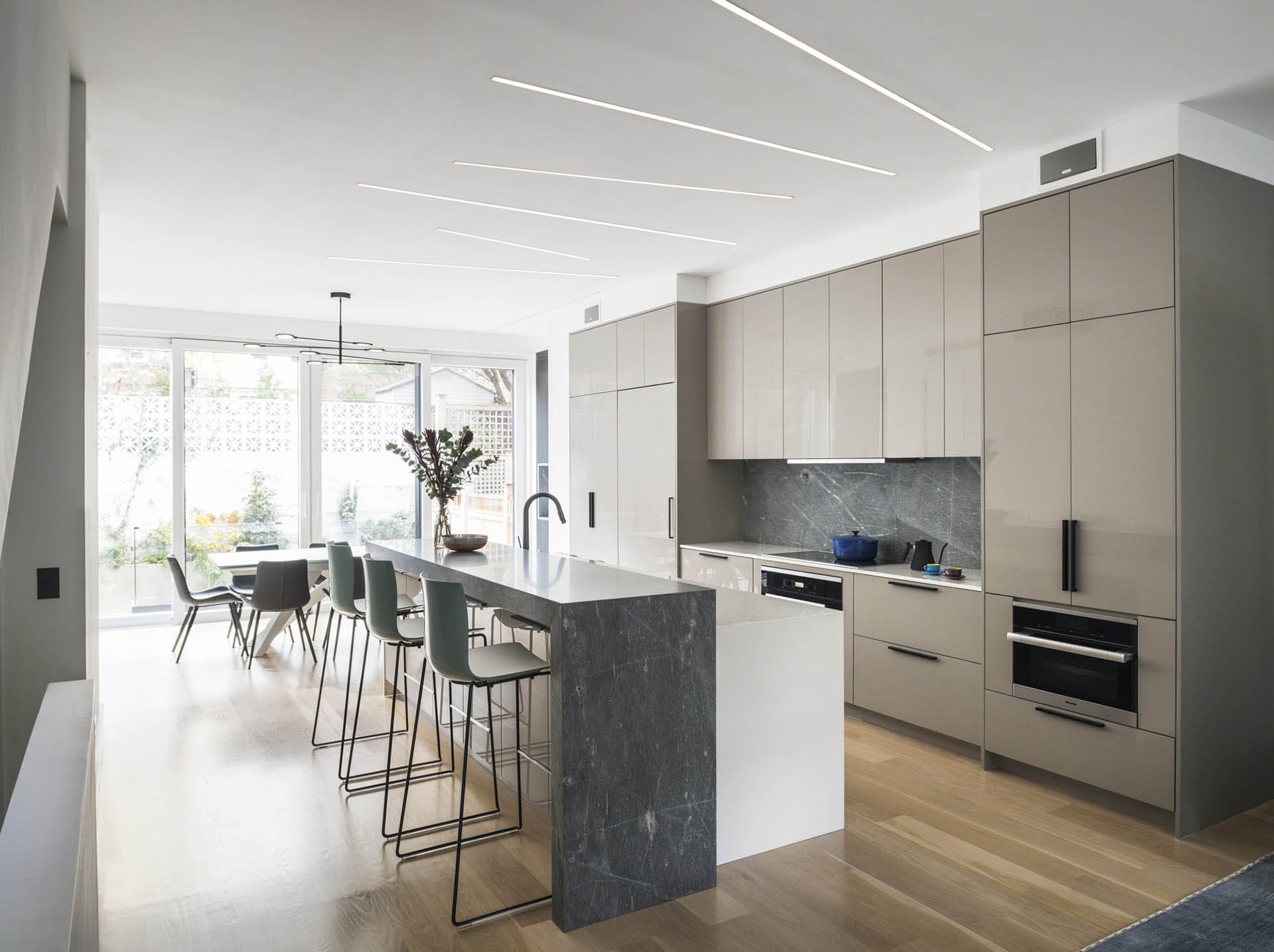 Parlor-level kitchen with wood floors, stone island and modern, tan cabinetry in a Brooklyn Heights Passive House