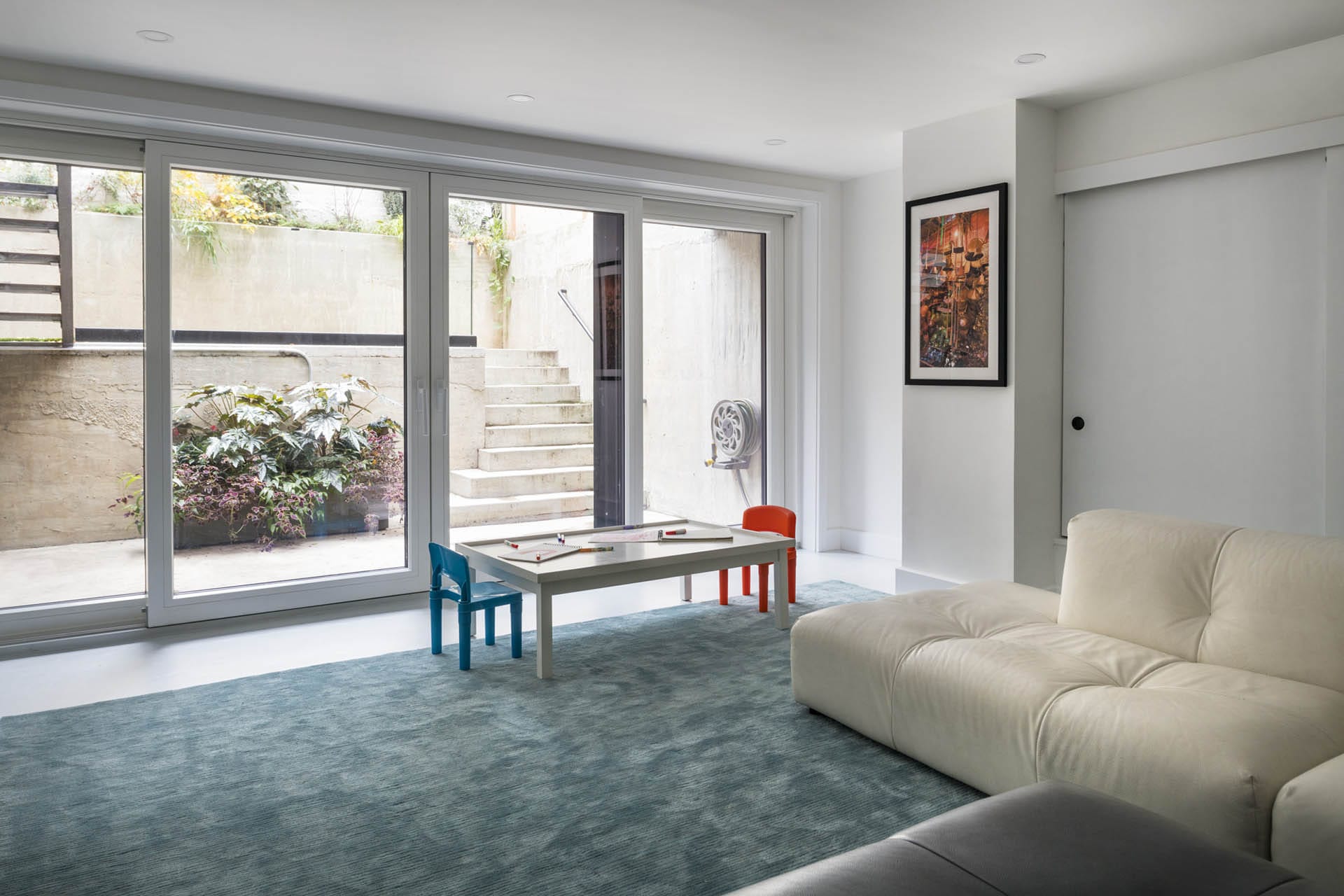 Play room with blue carpet, tan couch, and floor-to-ceiling sliding glass doors leading out to back yard.