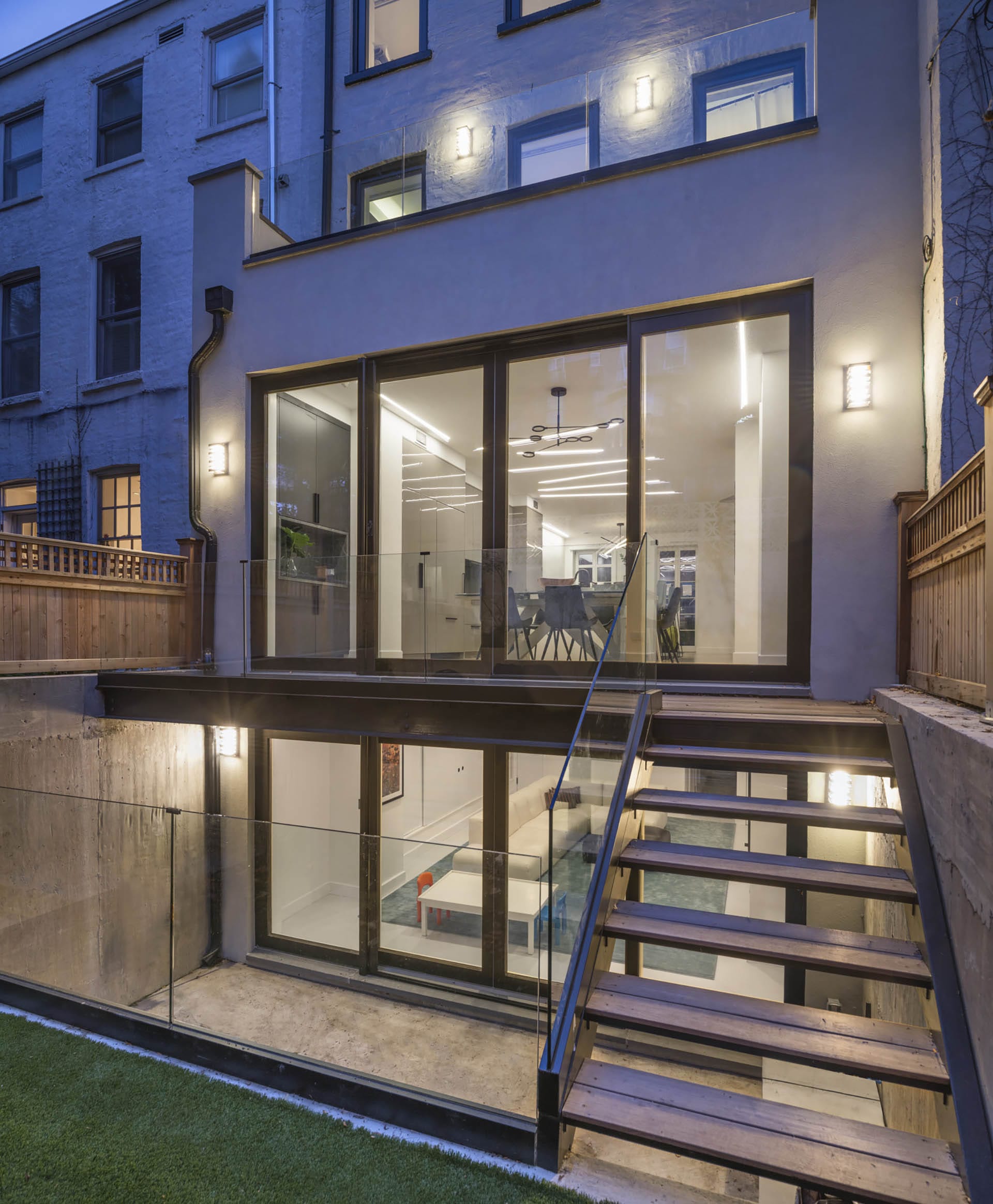 Rear facade of Brooklyn Heights Passive House at twilight, looking into the dining room and playroom through large glass doors.
