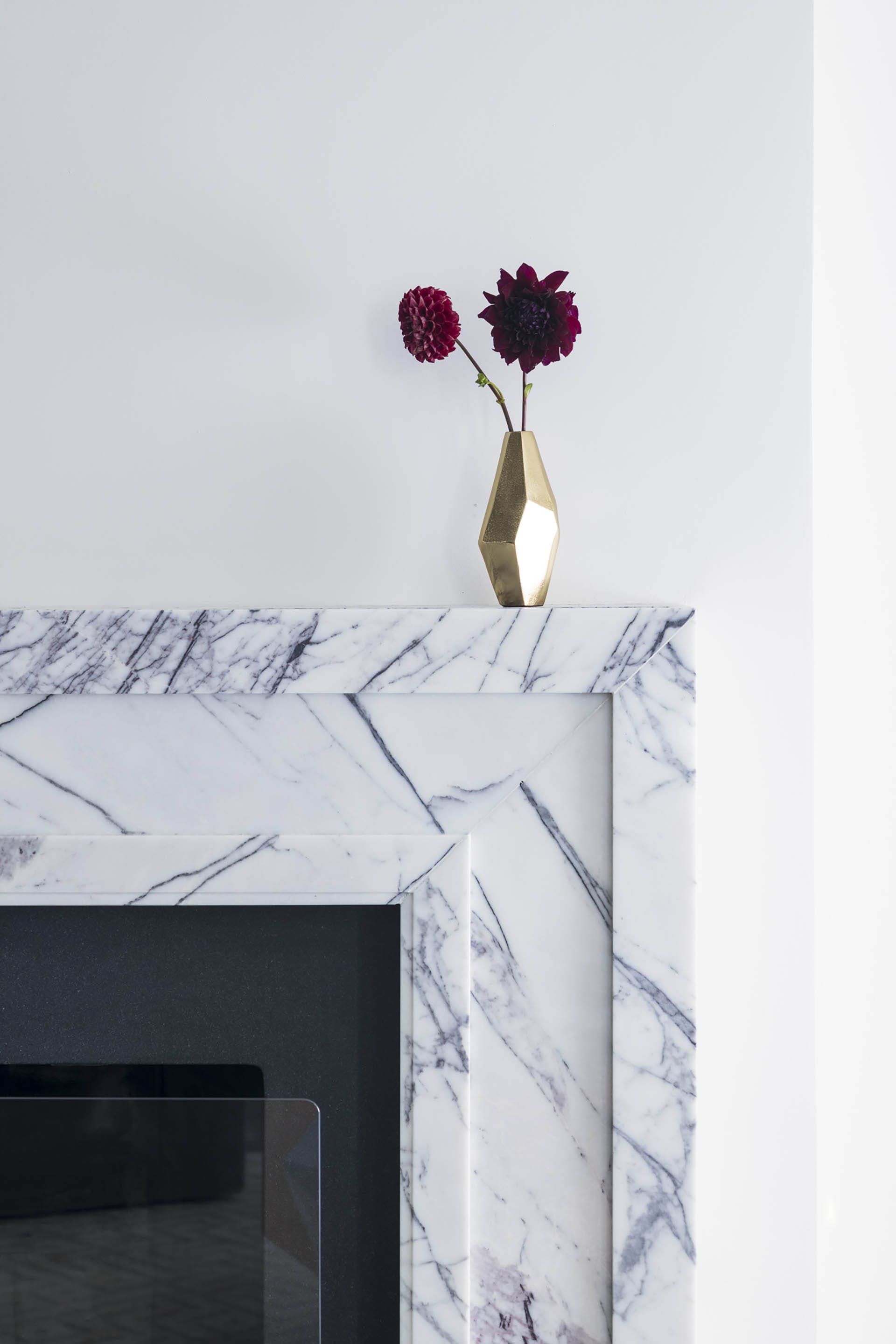 White marble mantel with a gold vase containing two pink flowers on top of it.